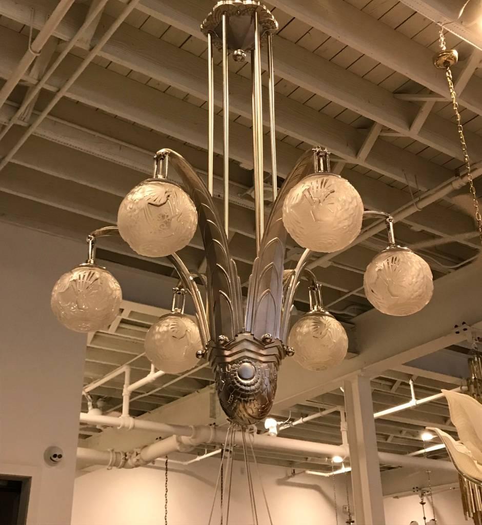 Stunning French Art Deco geometric chandelier signed by Muller Frères Luneville. Having six clear frosted glass globes or sphere with geometric and bird motif details. Supported by multi-tiered, sky scraper geometric polished nickel design frame.