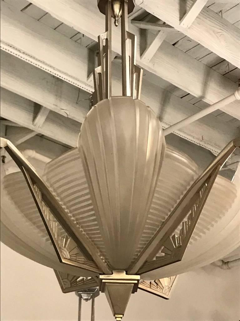 Stunning French Art Deco chandelier signed by Atelier Petitot. Having four clear frosted glass skyscraper panels with vertical and horizontal ribbed design details. Shades rests on a geometric Deco design frame plated in polish nickel ( silver). Has