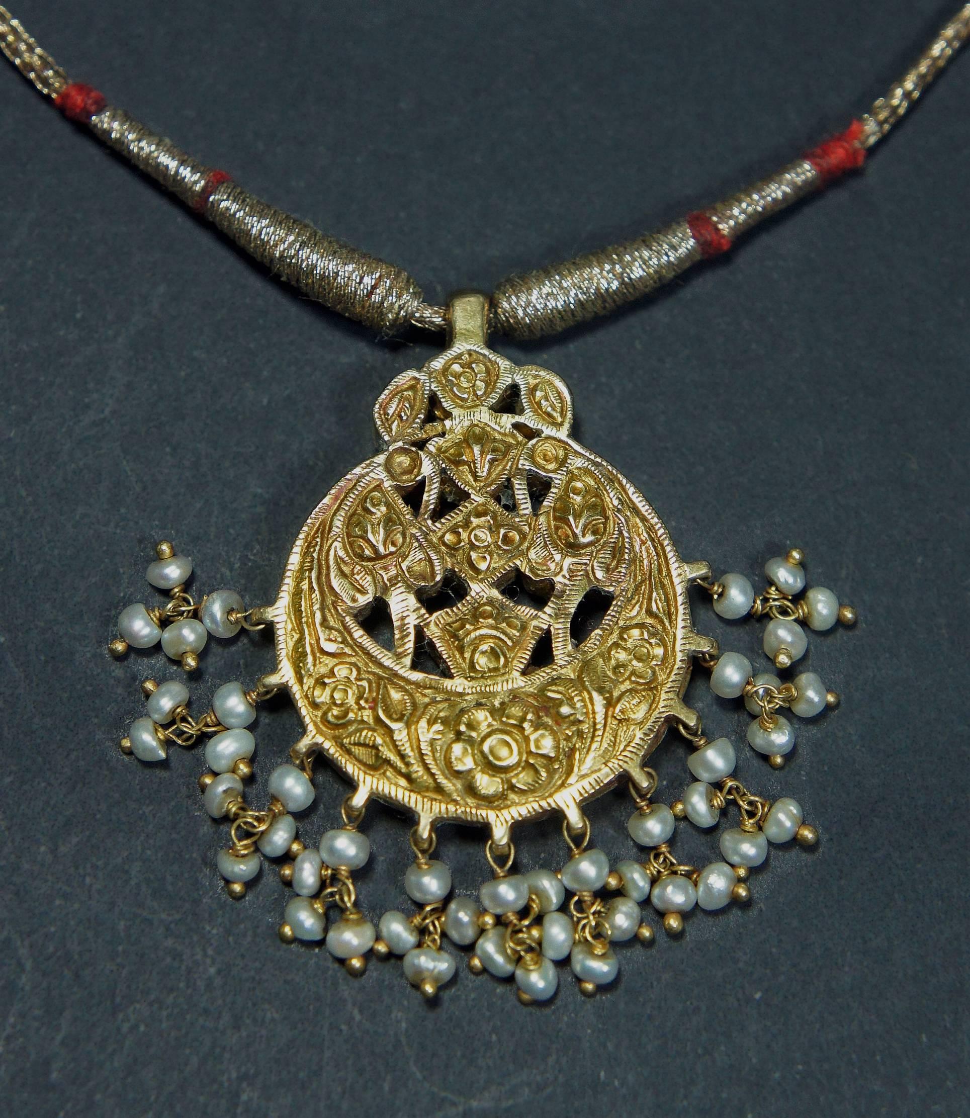 Mughal style reticulated work pendant. 22-karat gold, Basara pearls tassels, inlaid with rubies, emeralds in 22-karat gold kundan technique with repousse floral pattern on the back with gold cord.