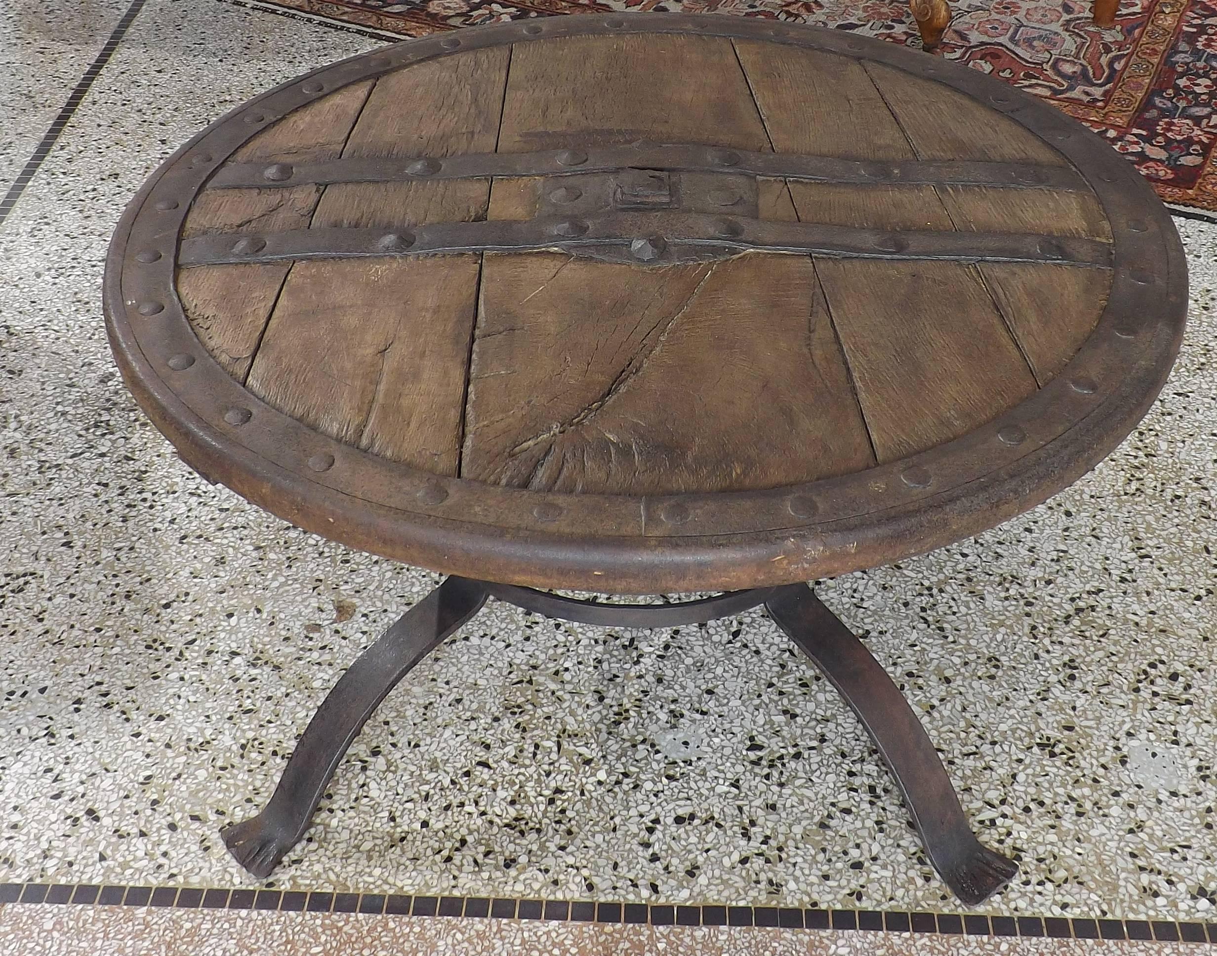 Heavy sturdy wheel dating from the middle ages of European origin. Hand-forged riveted rim with iron cross straps on both sides. Also included is a handsome hand-wrought base, circa 1900 for display or to use as a coffee table.