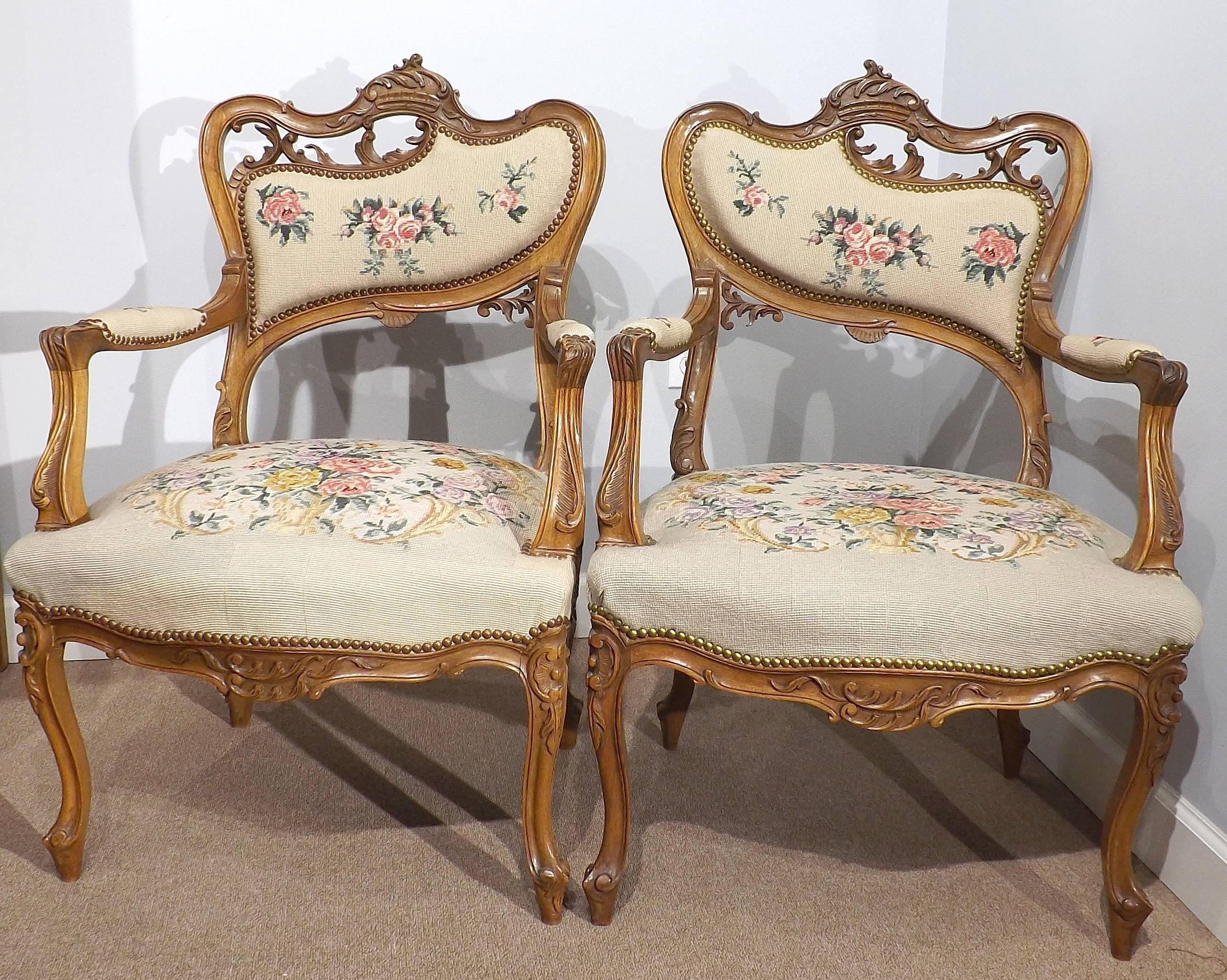 Hand-carved walnut fauteuils in Louis XV style with Art Nouveau subtleties consistent with their time manufacture. Covered with a floral needlepoint tapestry. 

Early professional restoration of tapestry on one of the seats, see pictures.