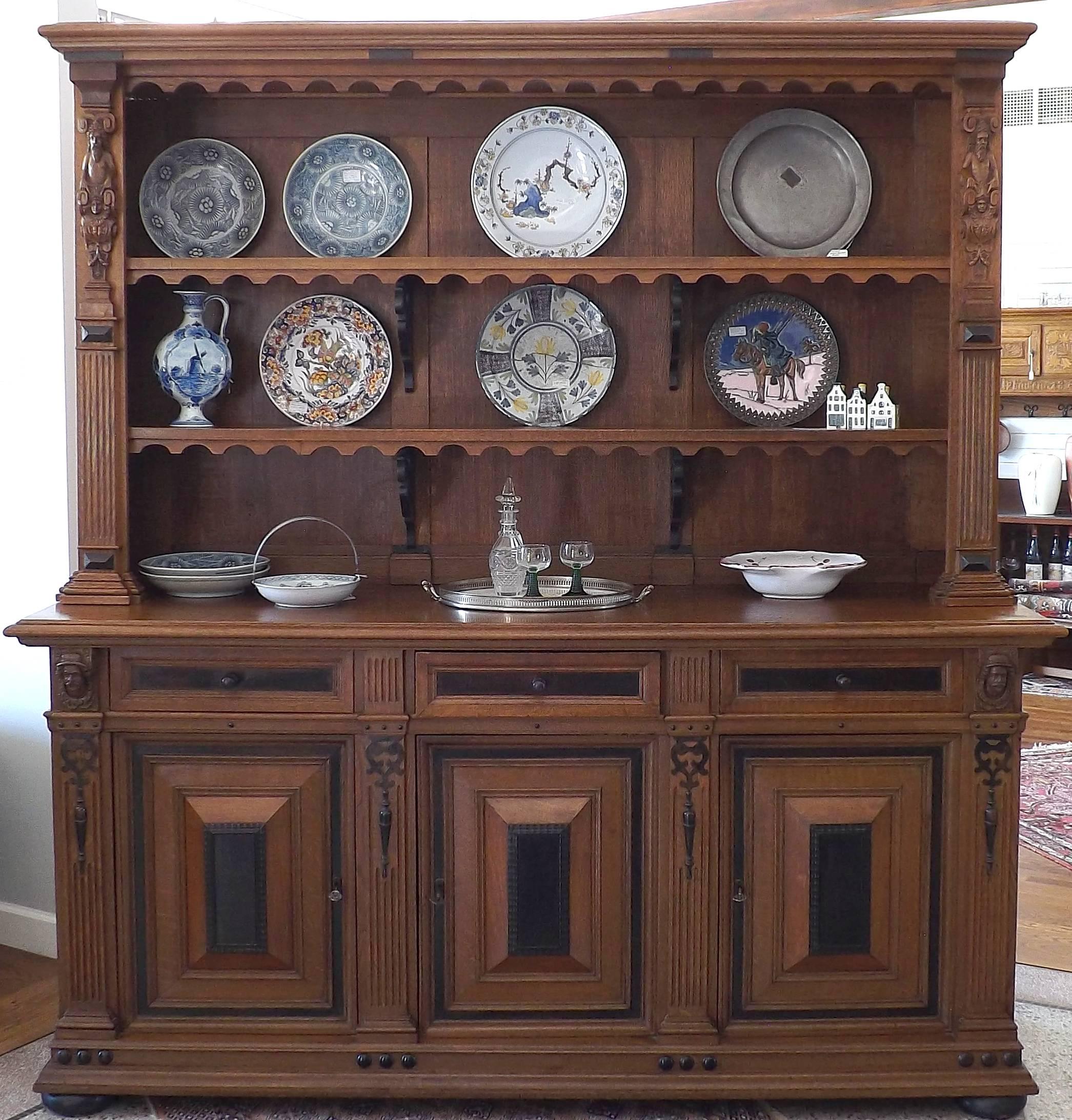 A beautifully accented three-door cabinet of oak and ebonized wood highlighted with carved figures. This grand piece has scrolled supports for the center shelving which has a plate rack notch, while the body of the cabinet rest on black bun feet.