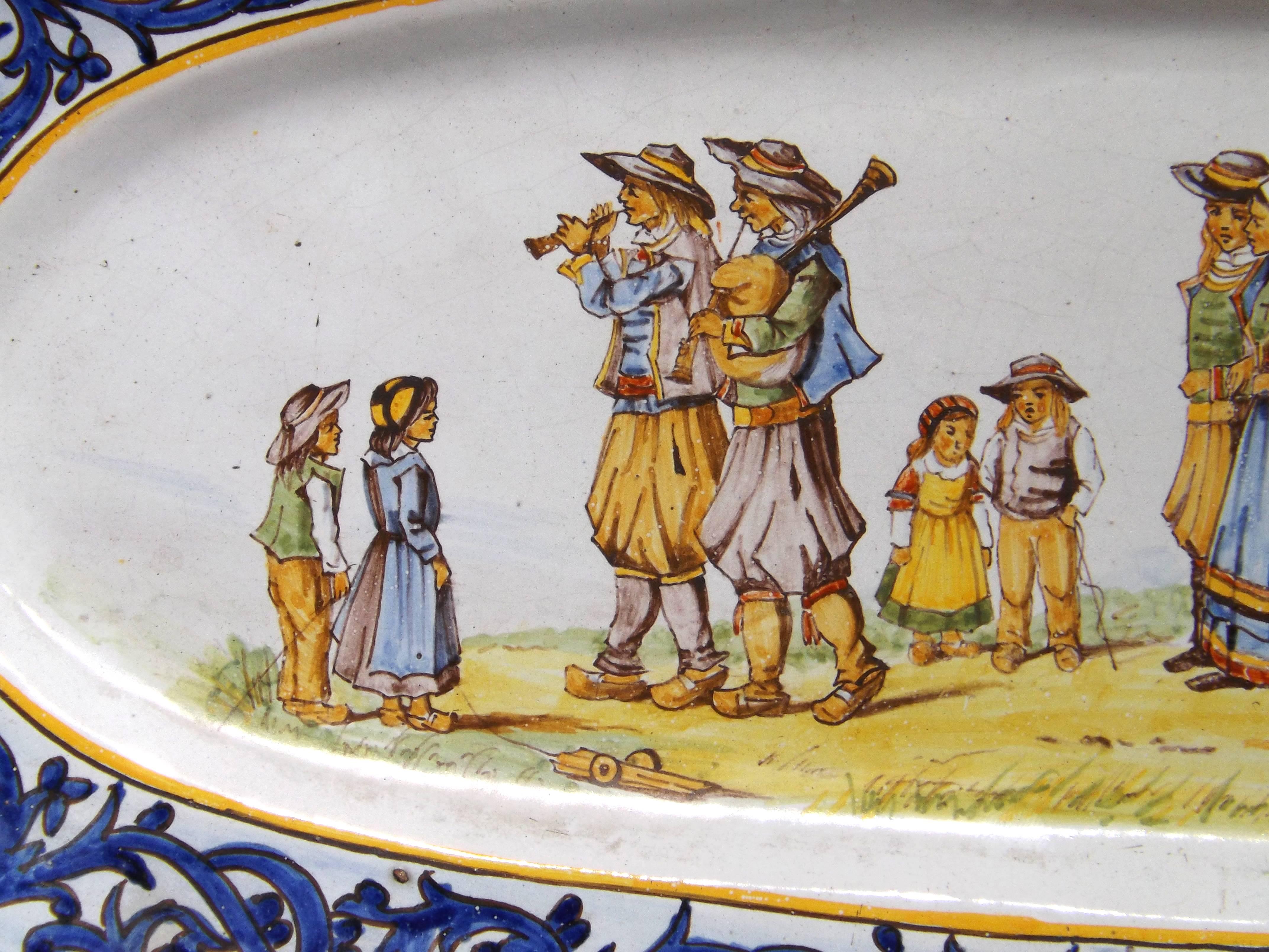 A large platter decorated with a peasant wedding surrounded by blue scroll-work. Marked on the bottom with the HR underline mark, indicating it was decorated by Camille Moreau, a painter original at the Porquier factory trained by Alfred Beau. In