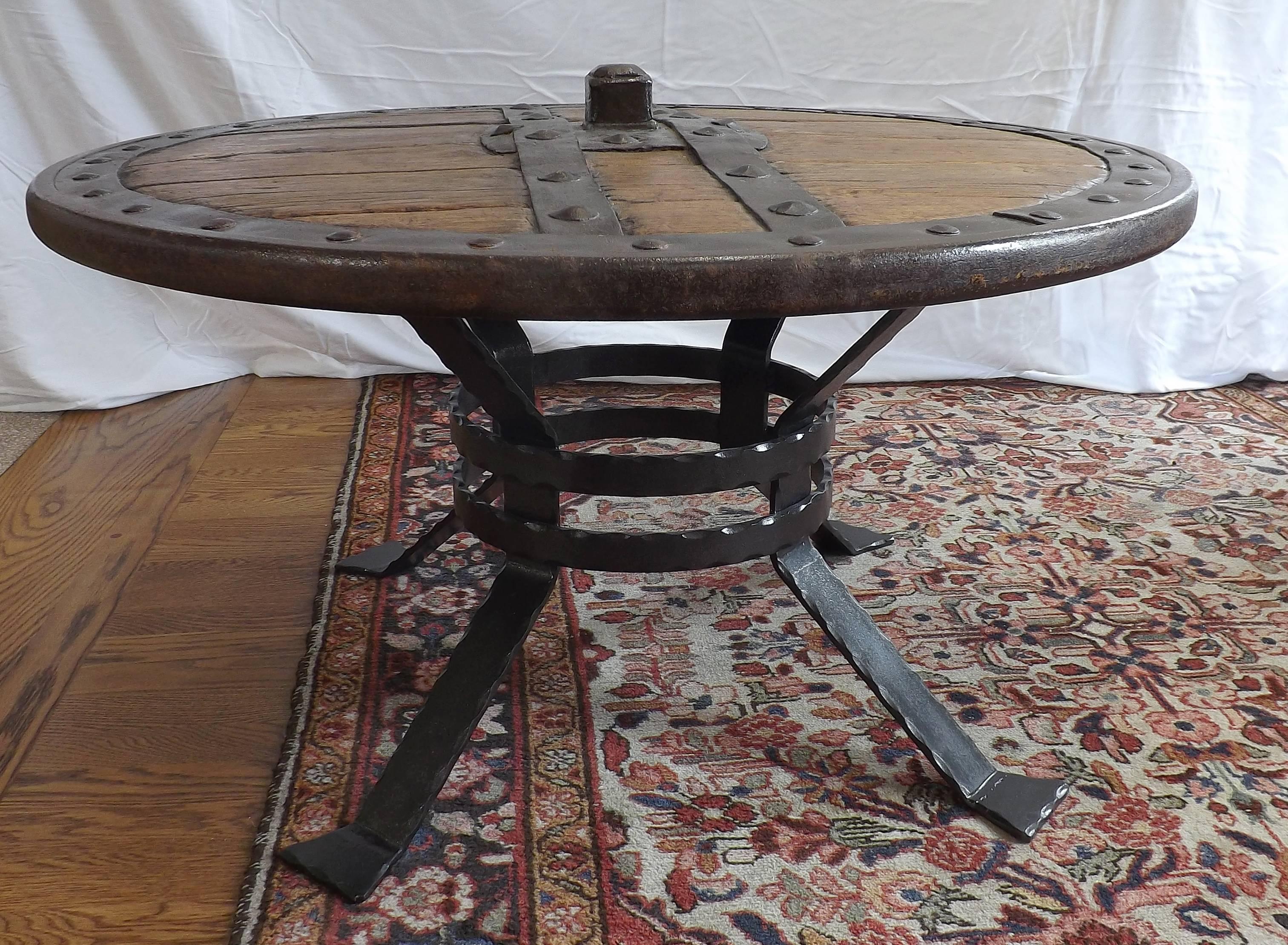 Heavy sturdy wheel dating from the middle ages of European origin. Hand-forged riveted rim with iron cross straps on both sides. The tabletop is 18 inches tall at the edge and a diameter of 33 1/20 inches. Also included is a handsome recently