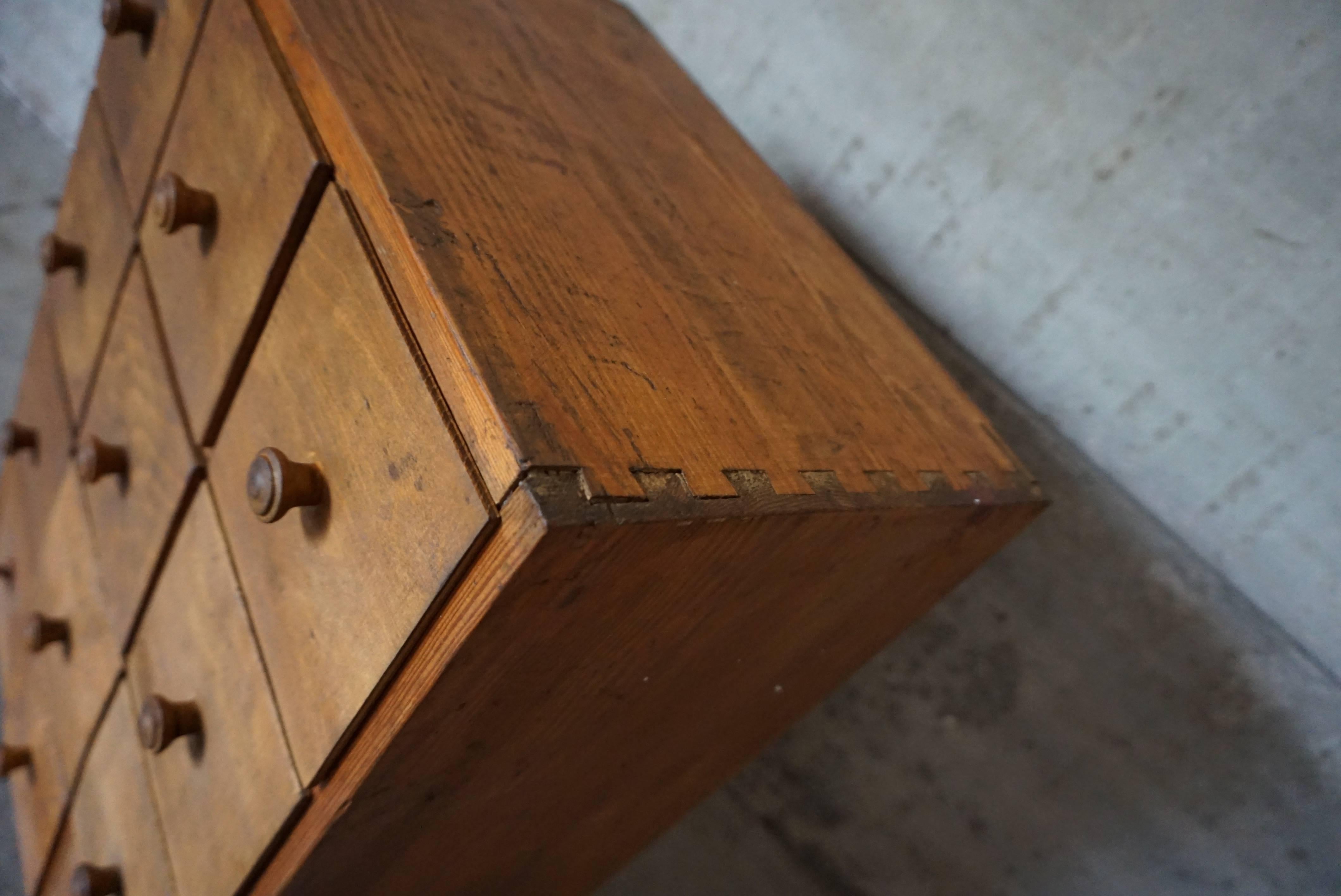 This Industrial tool cabinet was designed during the 1920s and manufactured in Germany. This cabinet features a pinewood frame with four columns of three drawers. The bottom left and right are glued to the frame so they can't be opened. It is in a
