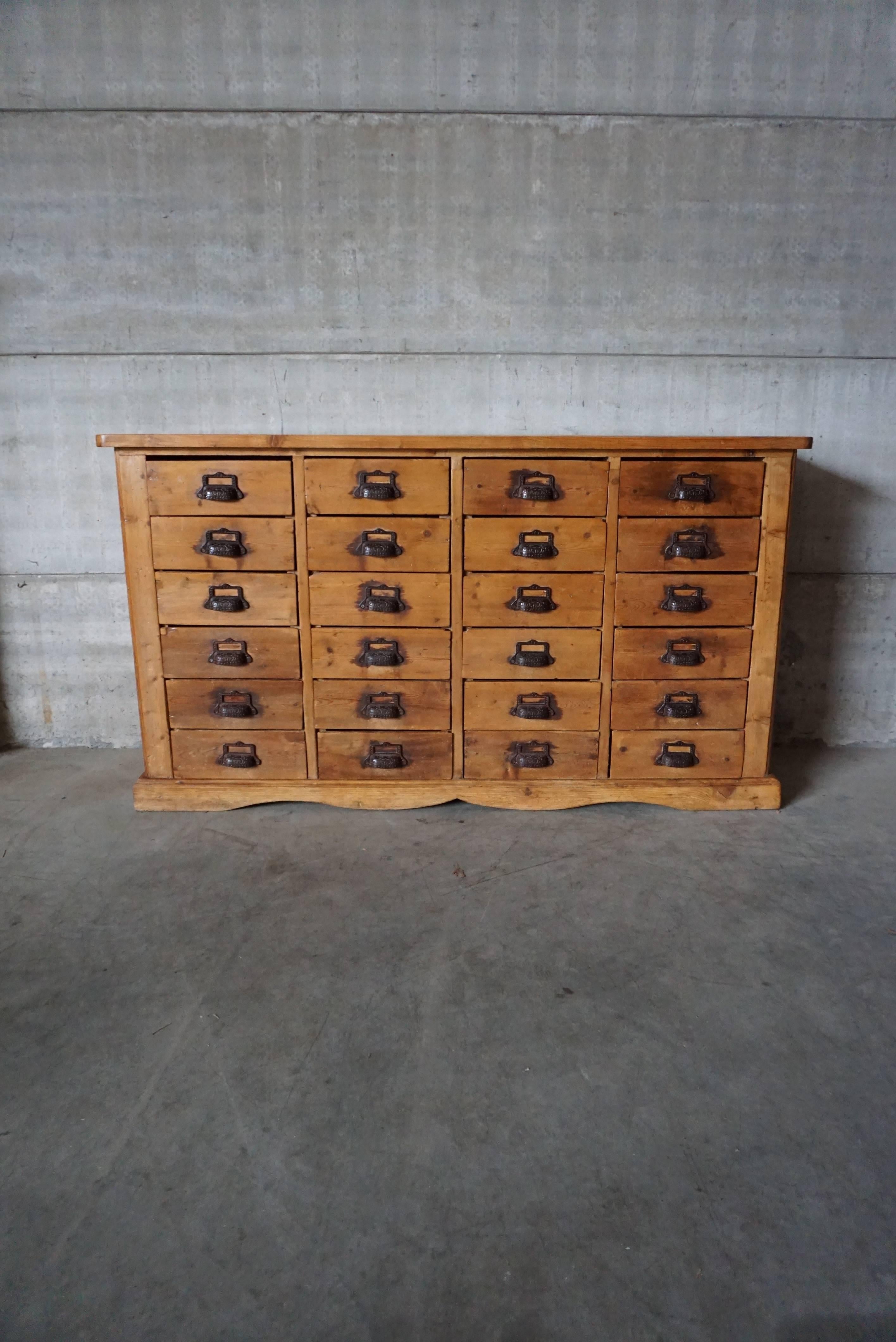 This apothecary bank of drawers was designed and made in circa 1900. It is made from pine with cast iron handles. The cabinet has retained a rich patina with some natural distressing.