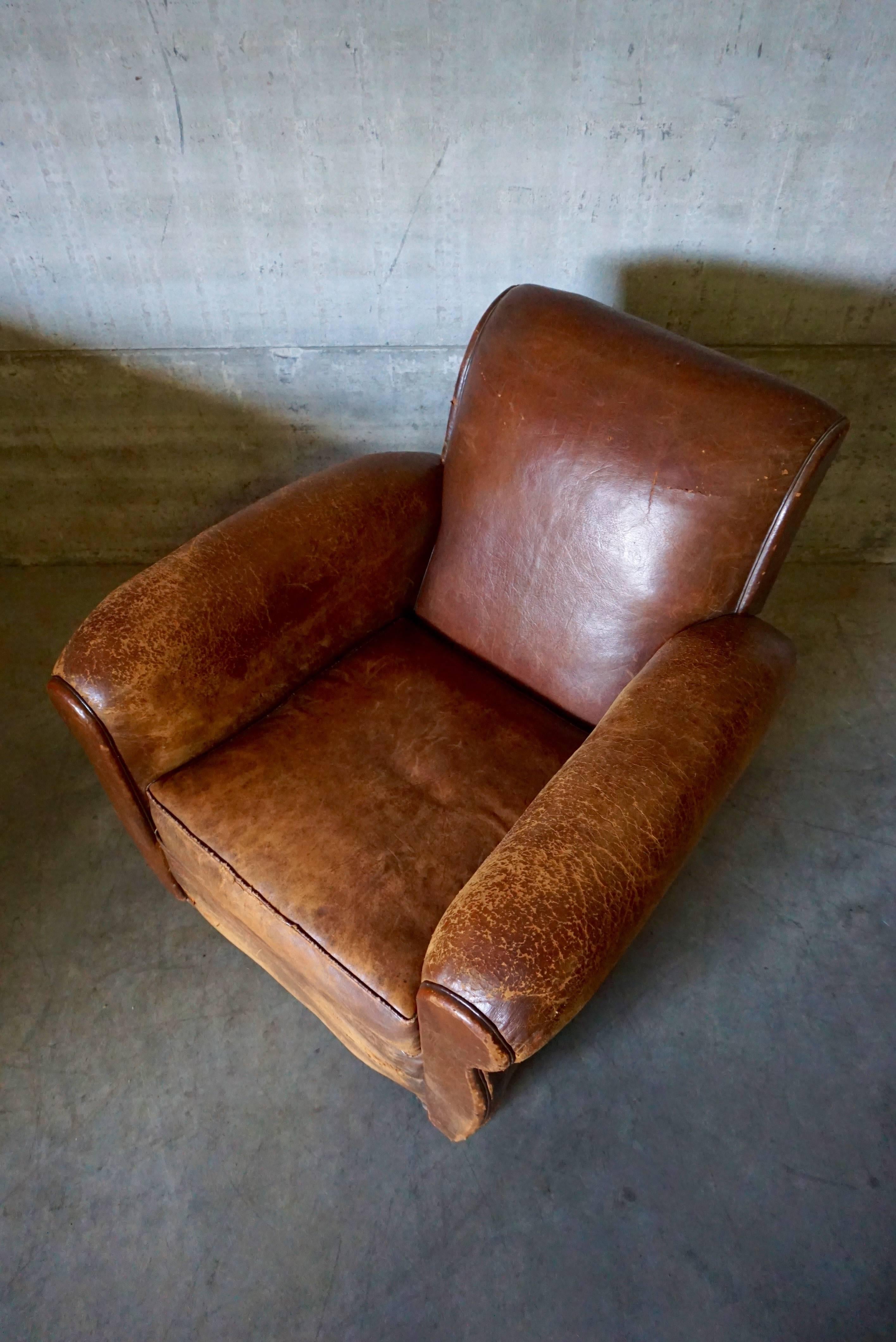 This club chair was designed and produced in France during the 1930s. The chair is made from cognac leather held together with metal pins and mounted on wooden legs. The lounge chair remains in a good vintage distressed condition with signs of use