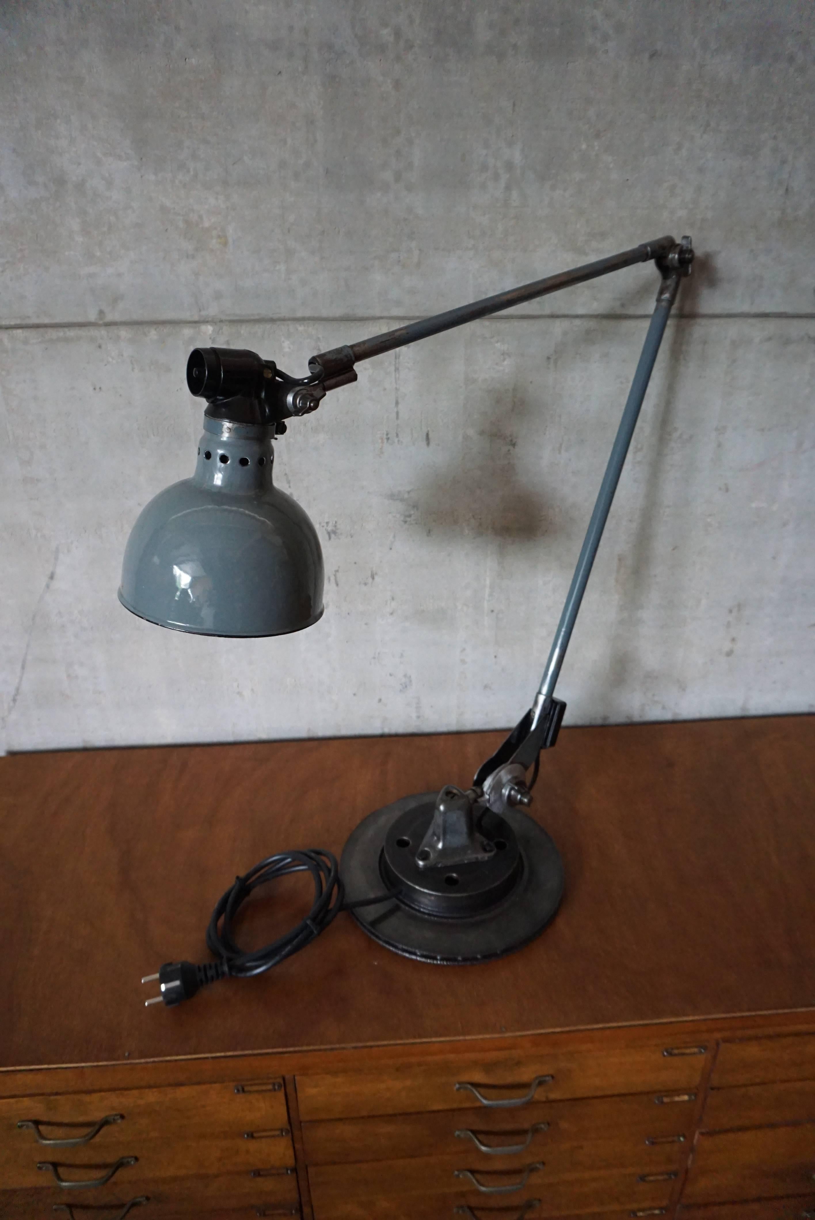 This Industrial desk lamp was designed by Ernst Rademacher in the early 20th century and manufactured by Rademacher in the 1930s. It features a large, blue enamel lampshade mounted on a brake disk which is later added for stability. It is marked