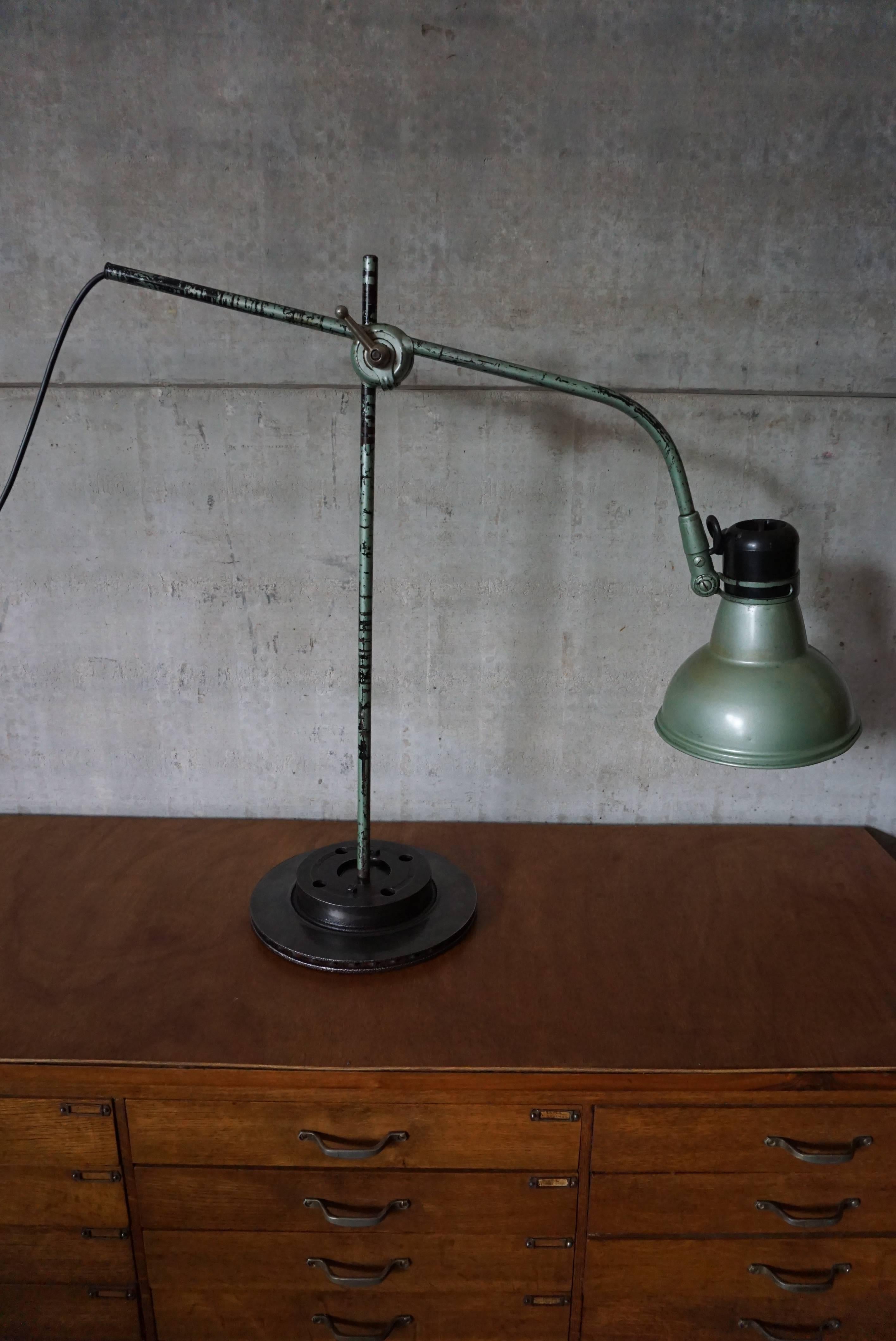 This industrial desk lamp was designed and manufactured by ERPE Belgium in the 1950s. It features a large, green lampshade mounted on a brake disk which is later added for stability. It is marked with the manufacturer's stamp and has been recently