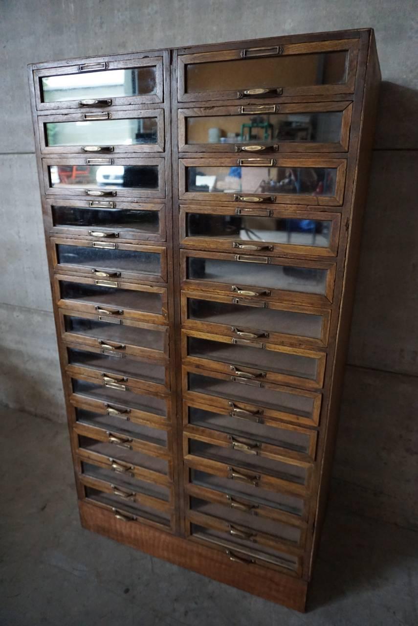 This vintage haberdashery shop cabinet originates from the United Kingdom. It is made from wood and features 26 glass fronted drawers. The cabinet is in a good vintage condition with the drawers opening and shutting smoothly.