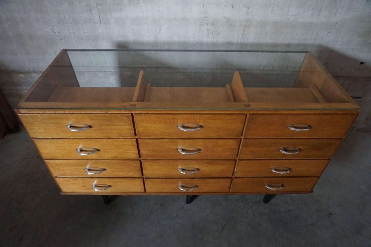 This small shop counter was made and manufactured during the 1950s. It features a wooden frame, drawers and a glass casing. It remains in a good vintage condition with some marks consistent with age and use.