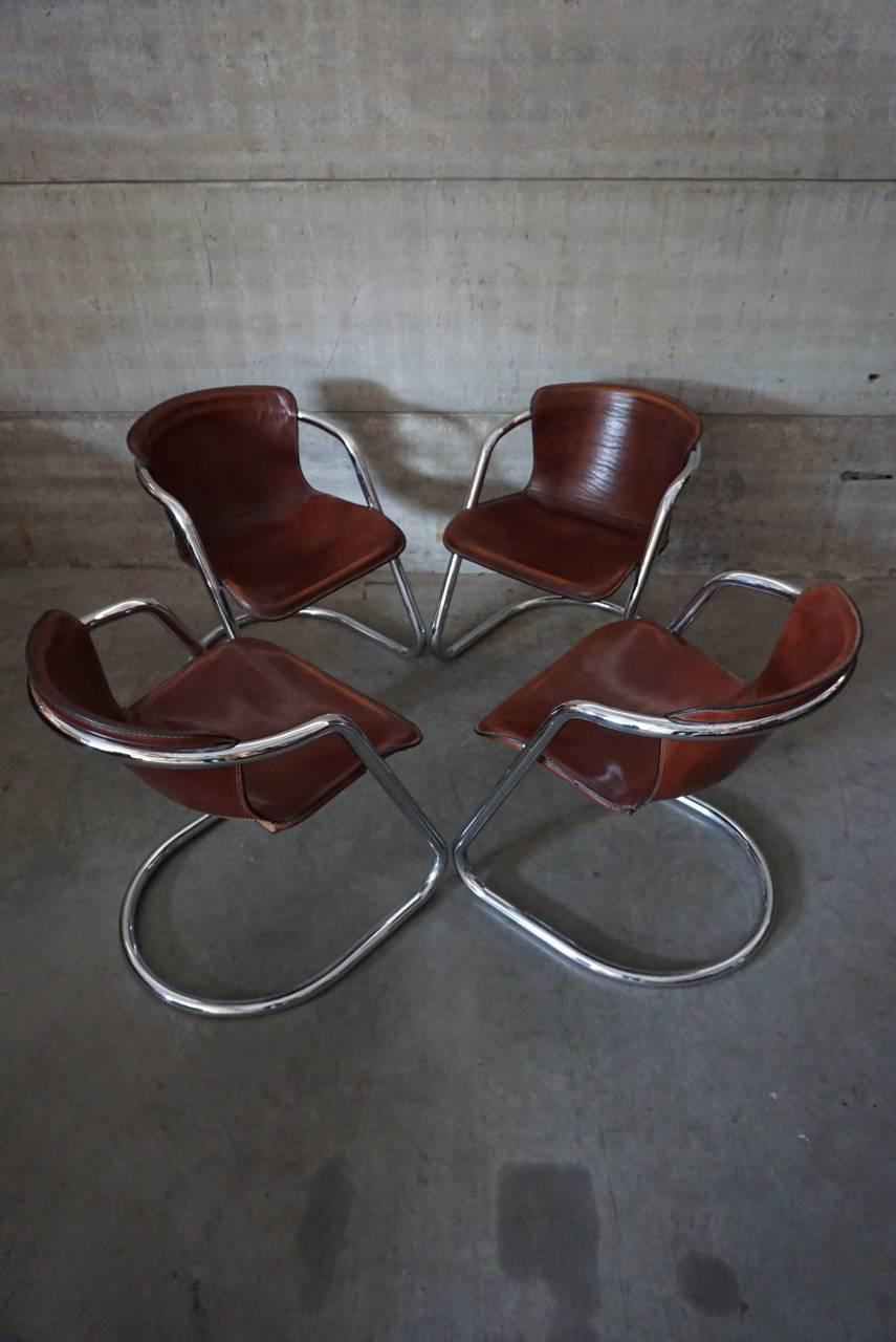 This set of four dining chairs were designed by Willy Rizzo in the 1970s. They feature a chrome tubular frame with thick cognac leather seats. They are in a good vintage condition with signs of use.