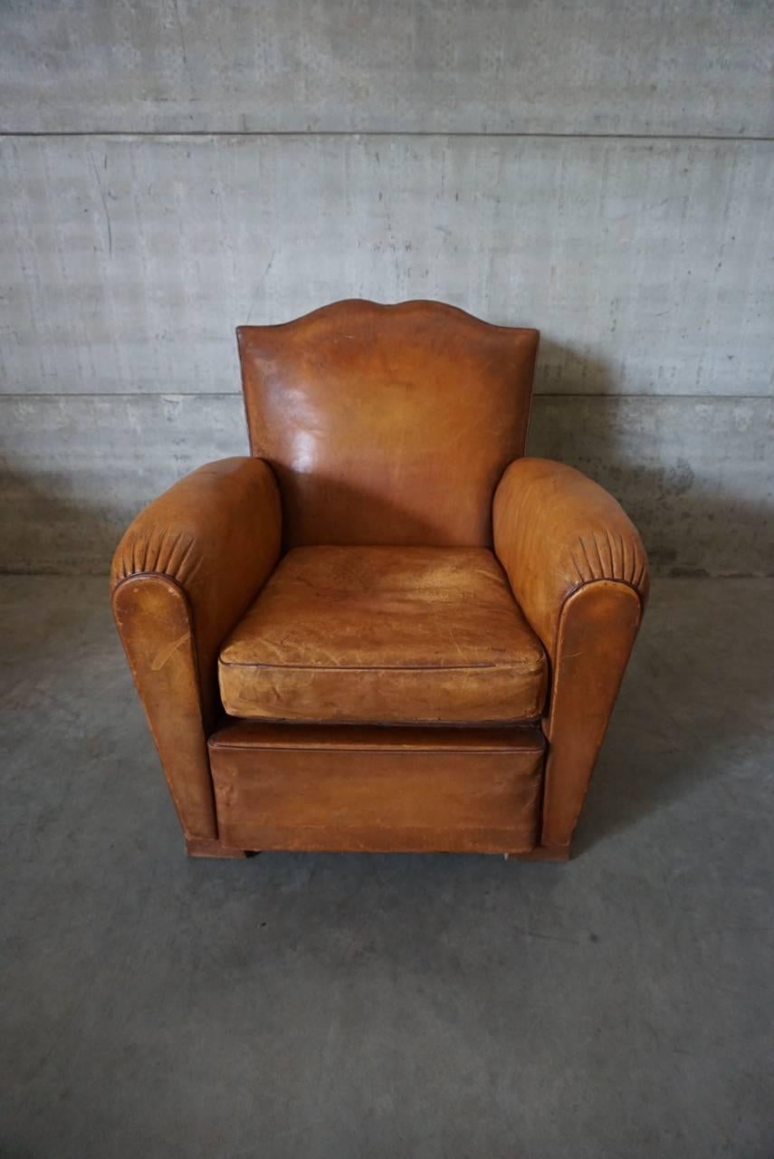 This club chair was designed and produced in France during the 1940s. The chair is made from cognac leather held together with metal pins and mounted on wooden legs. The lounge chair is in a fair vintage condition without rips.