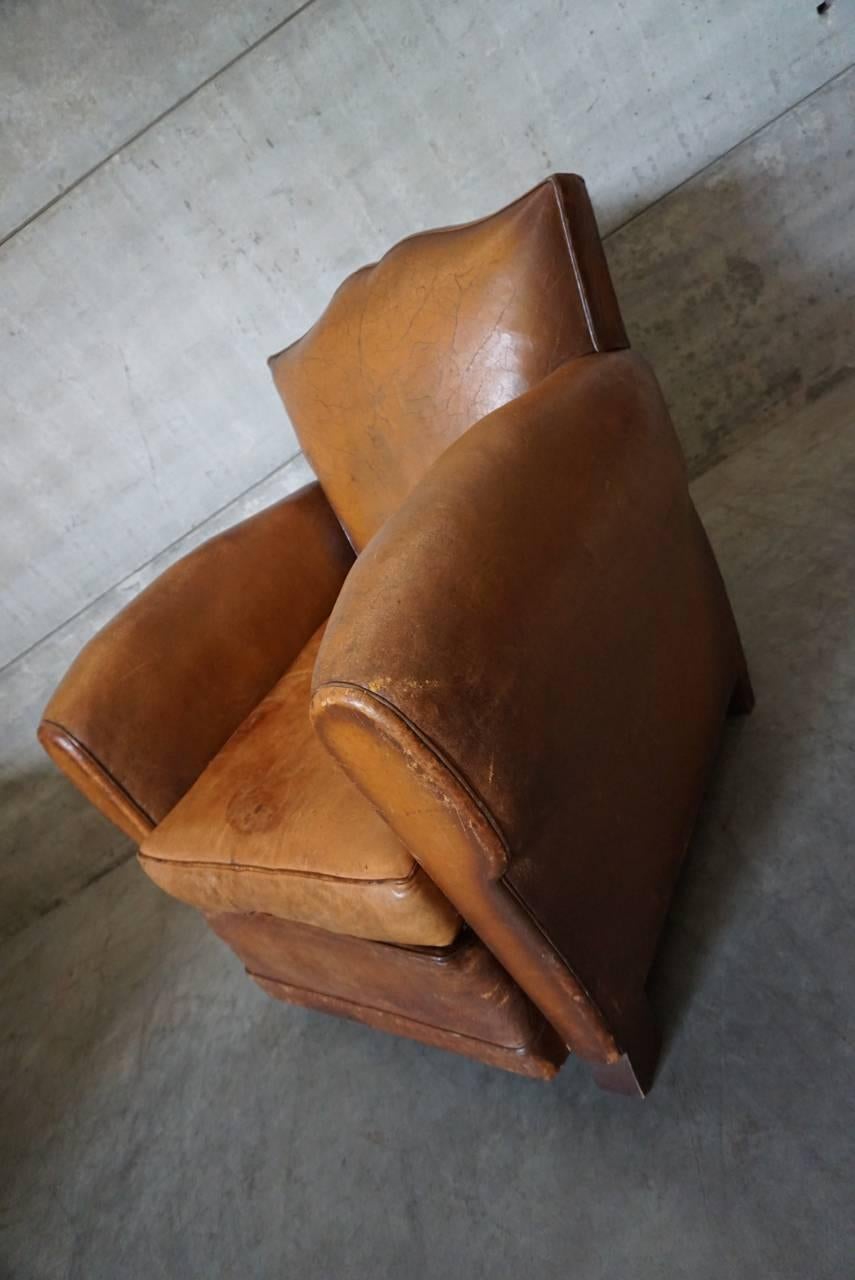 This club chair was designed and produced in France during the 1940s. The chair is made from cognac leather held together with metal pins and mounted on wooden legs. The lounge chair is in a fair vintage condition without rips.