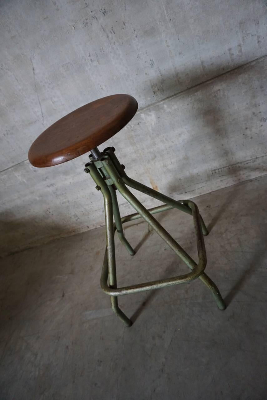 This French Industrial stool was made in France in the 1950s. It features a metal frame and a height-adjustable wooden seat.