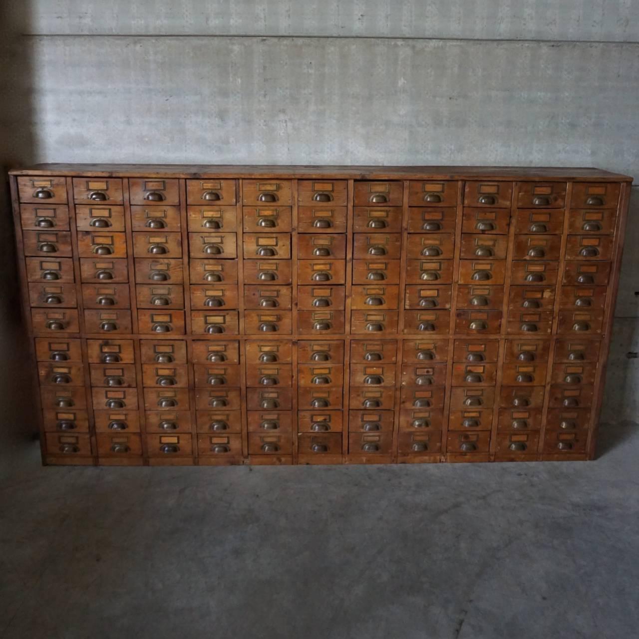 This restored apothecary bank of drawers was designed and made around the 1930s. It is made from pine and features 121 drawers with brass cup handles and name card holders.