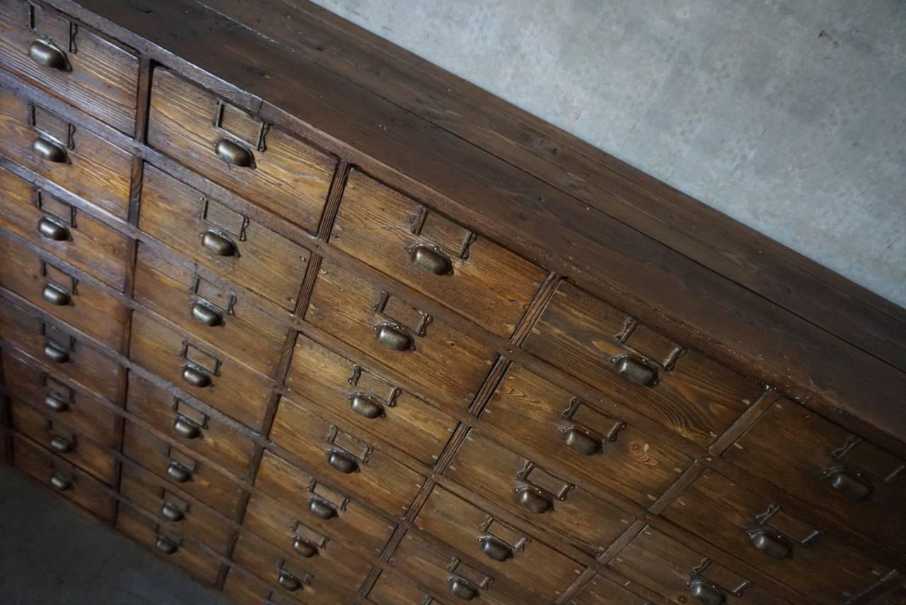 This apothecary bank of drawers was designed and made, circa 1920-1930. The piece is made from pine with cup handles. Some drawers have a divider which can be removed as a tray.