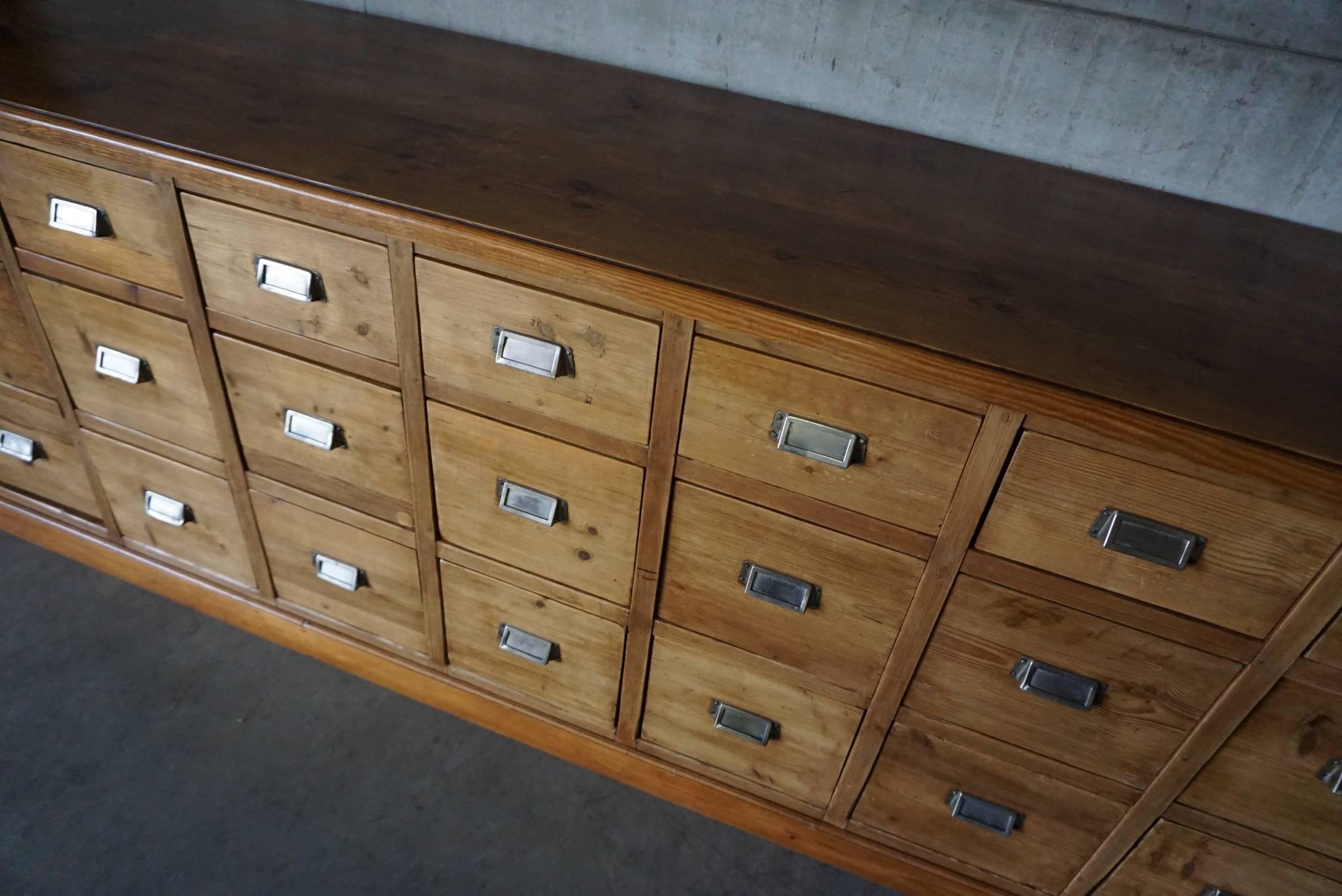This apothecary bank of drawers was designed and made around the 1950s. The piece is made from pine with cup handles.