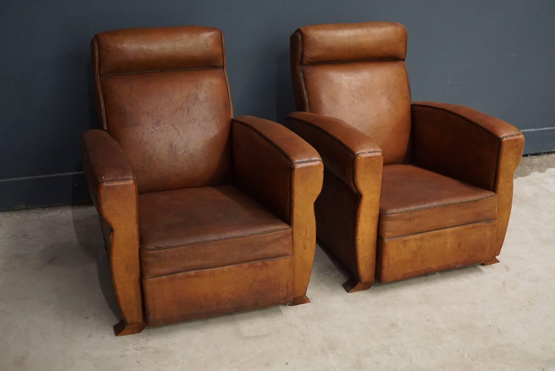 These club chairs were designed and produced in France during the 1940s. The chairs are made from cognac leather held together with metal pins and mounted on wooden legs. The chairs are in a vintage well used condition.