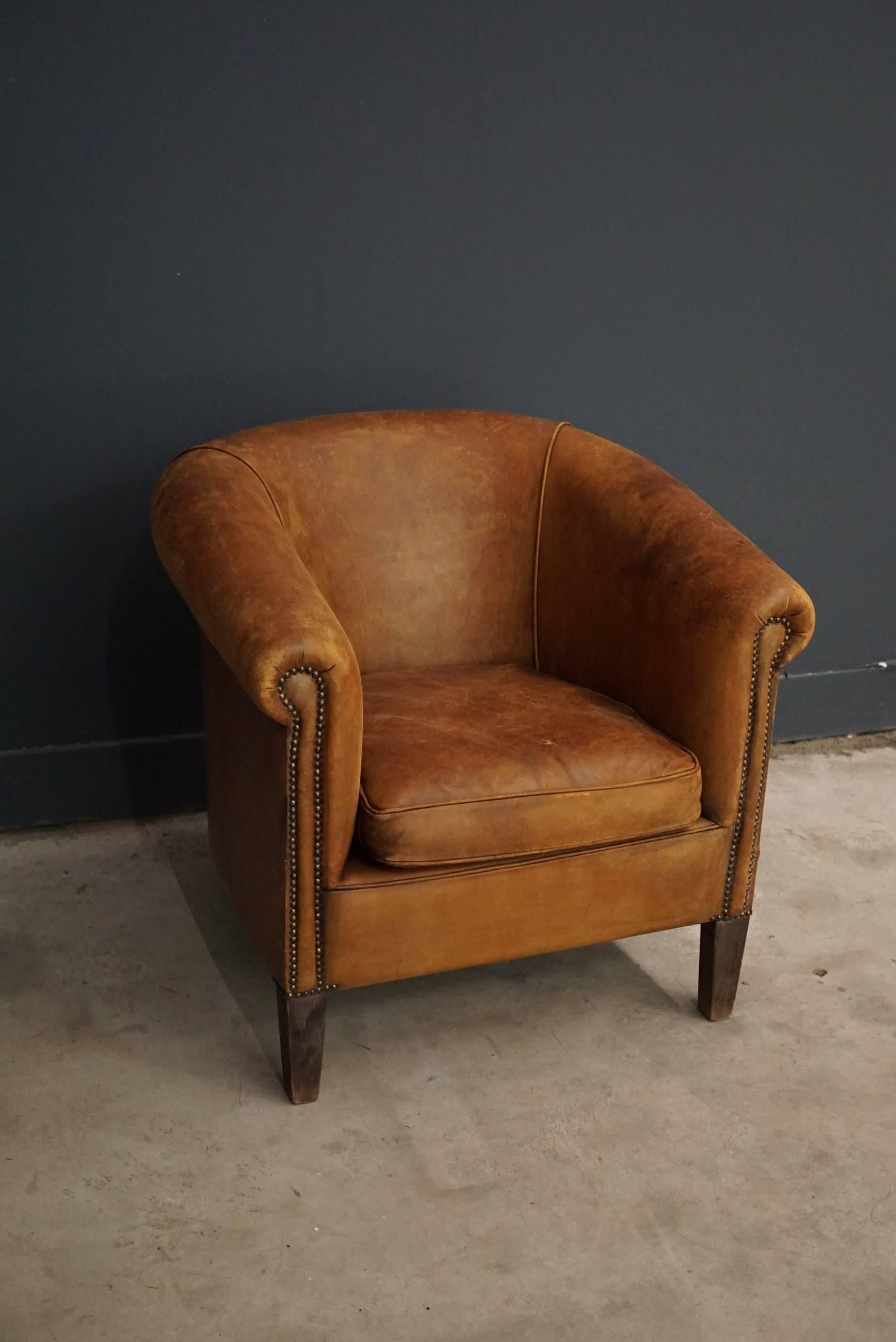 This club chair was designed and produced in France during the second half of the 20th century. The chair is made from cognac leather held together with metal pins and mounted on wooden legs. The lounge chair is in a vintage well used condition.