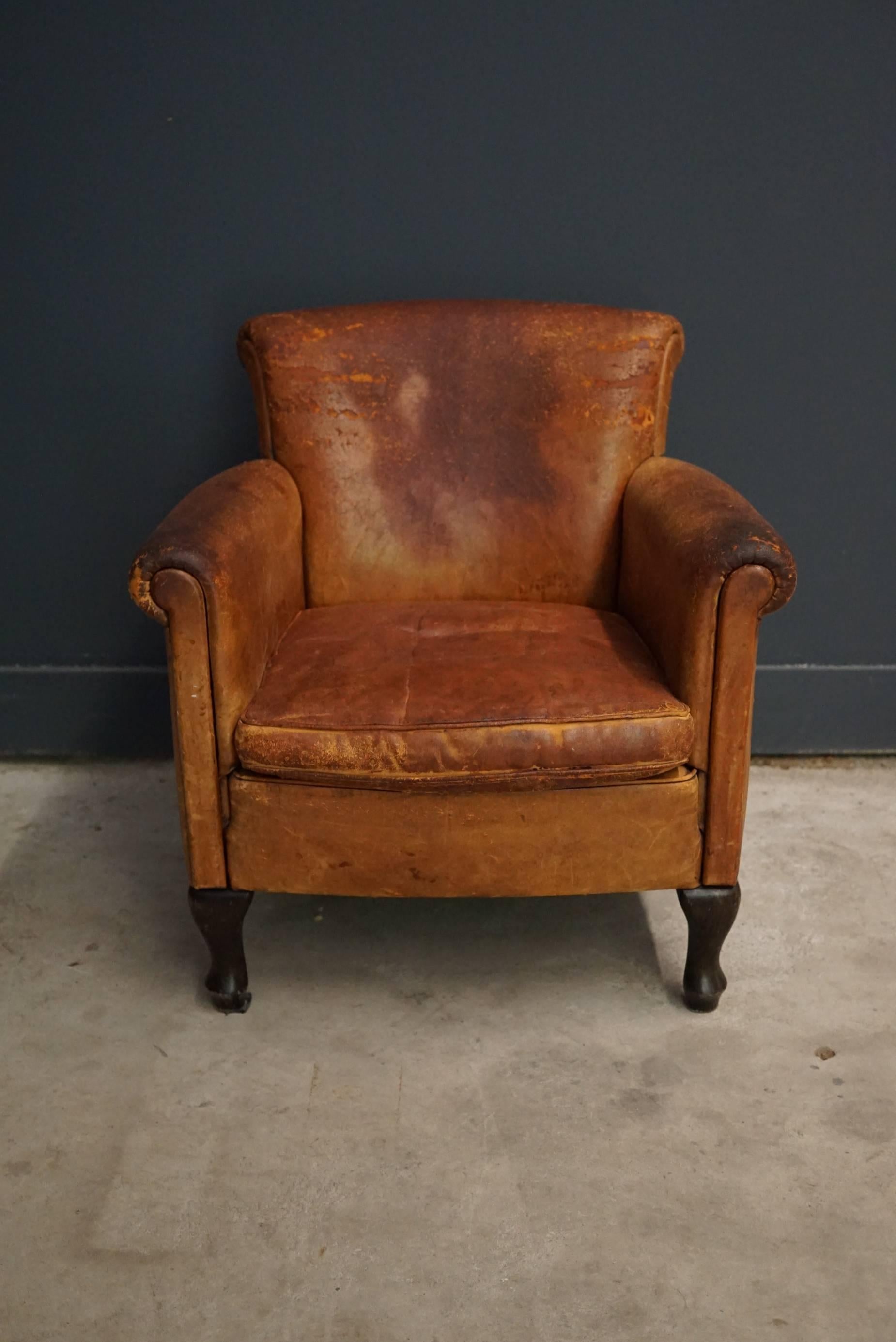 This club chair was designed and produced during the second half of the 20th century. The chair is made from cognac leather held together with metal pins and mounted on wooden legs. The lounge chair is in a vintage well used condition.