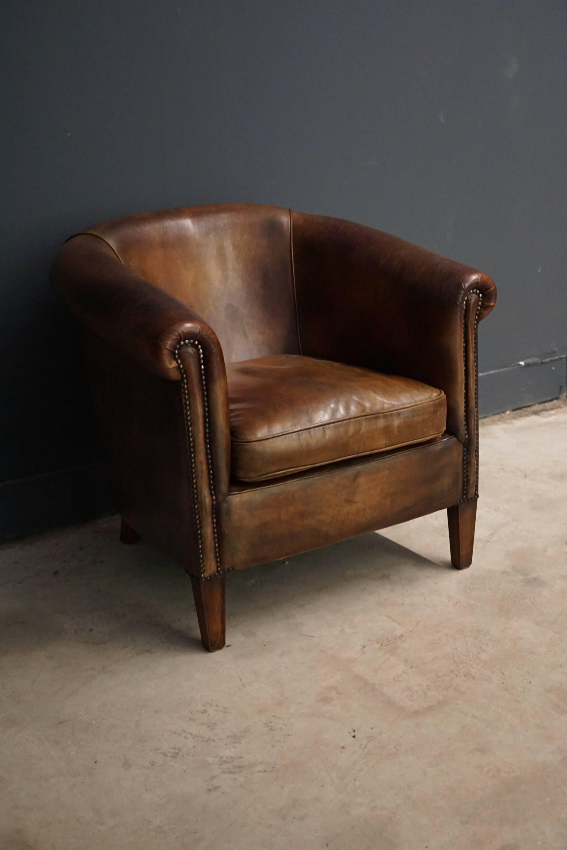 This club chair was designed and produced during the second half of the 20th century. The chair is made from cognac leather held together with metal pins and mounted on wooden legs. The lounge chair is in a vintage well used condition.