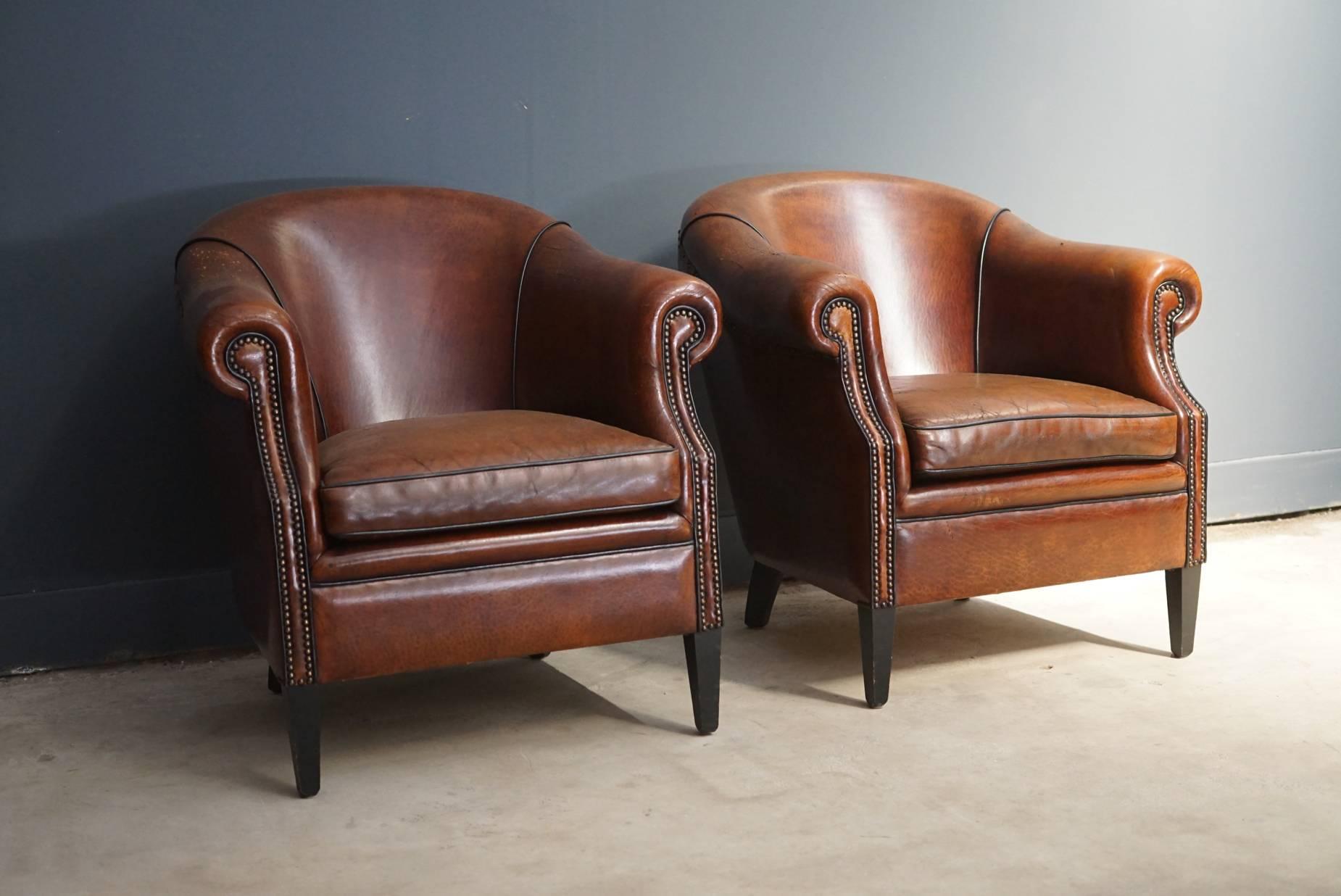 These club chairs were designed and produced in the Netherlands during the second half of the 20th century. The chairs are made from cognac leather held together with metal pins and mounted on wooden legs. The lounge chairs are in a vintage well