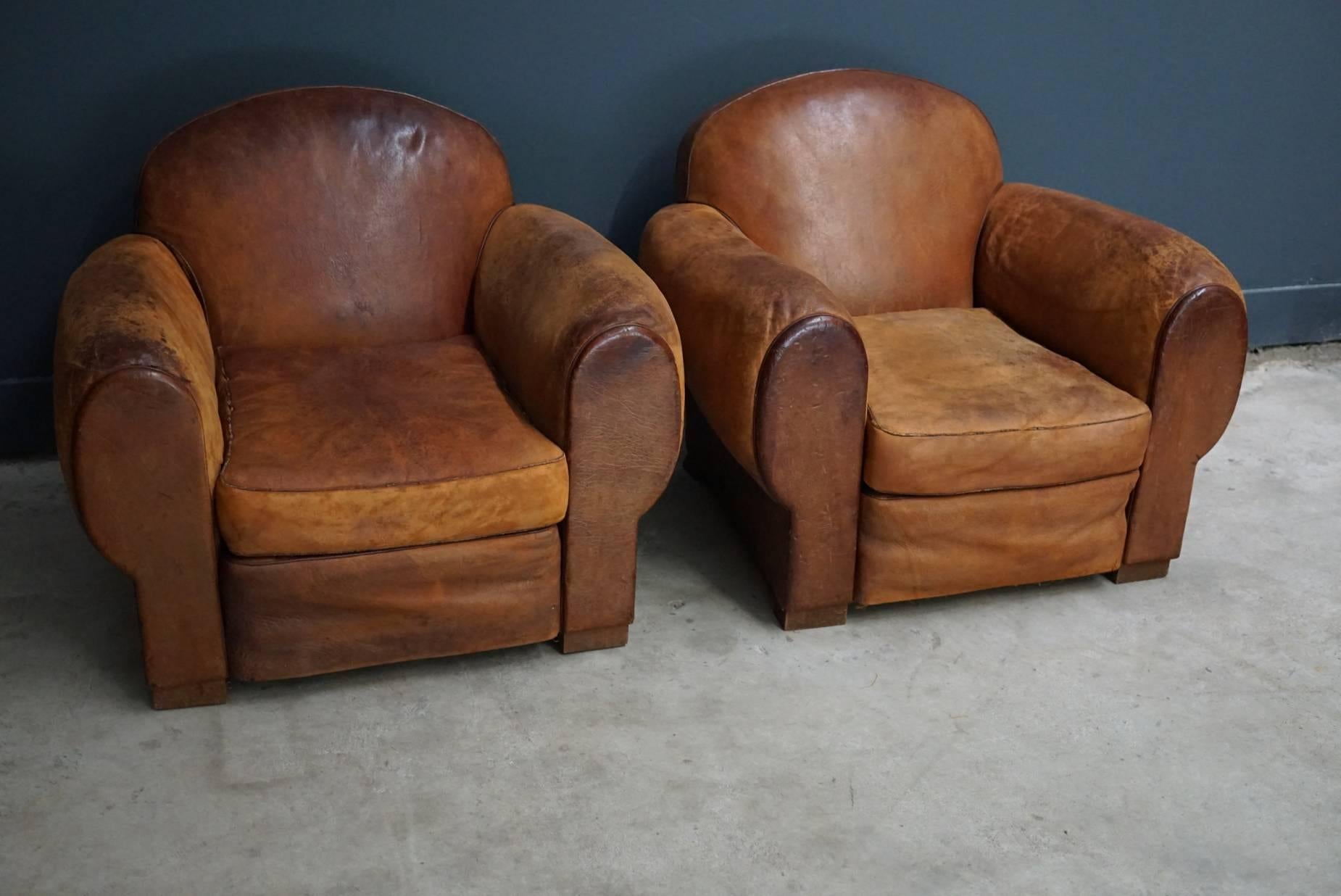 This pair of cognac-colored leather club chairs comes from France. They feature rivets and wooden legs.