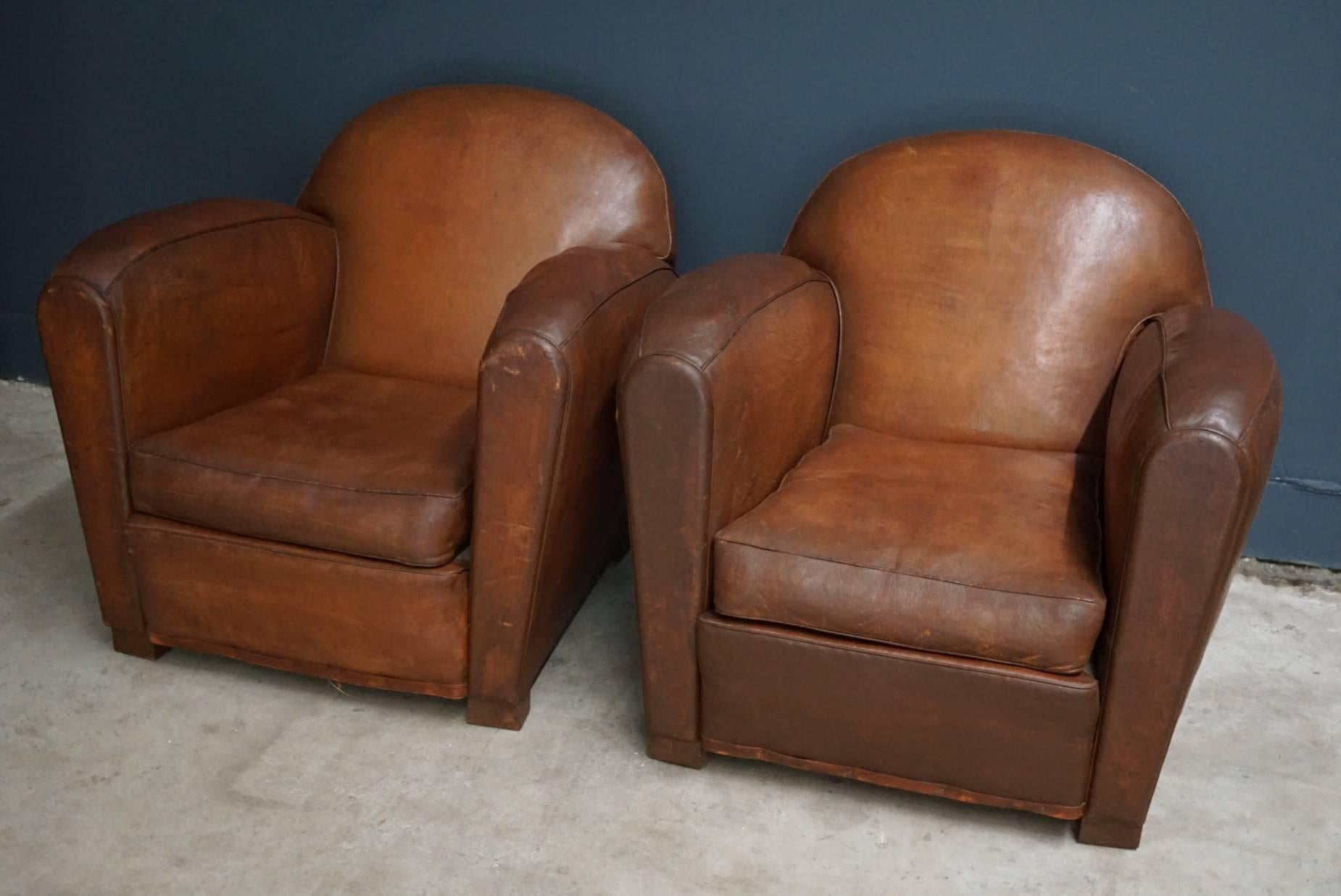 This pair of cognac-colored leather club chairs comes from France. They feature rivets and wooden legs.