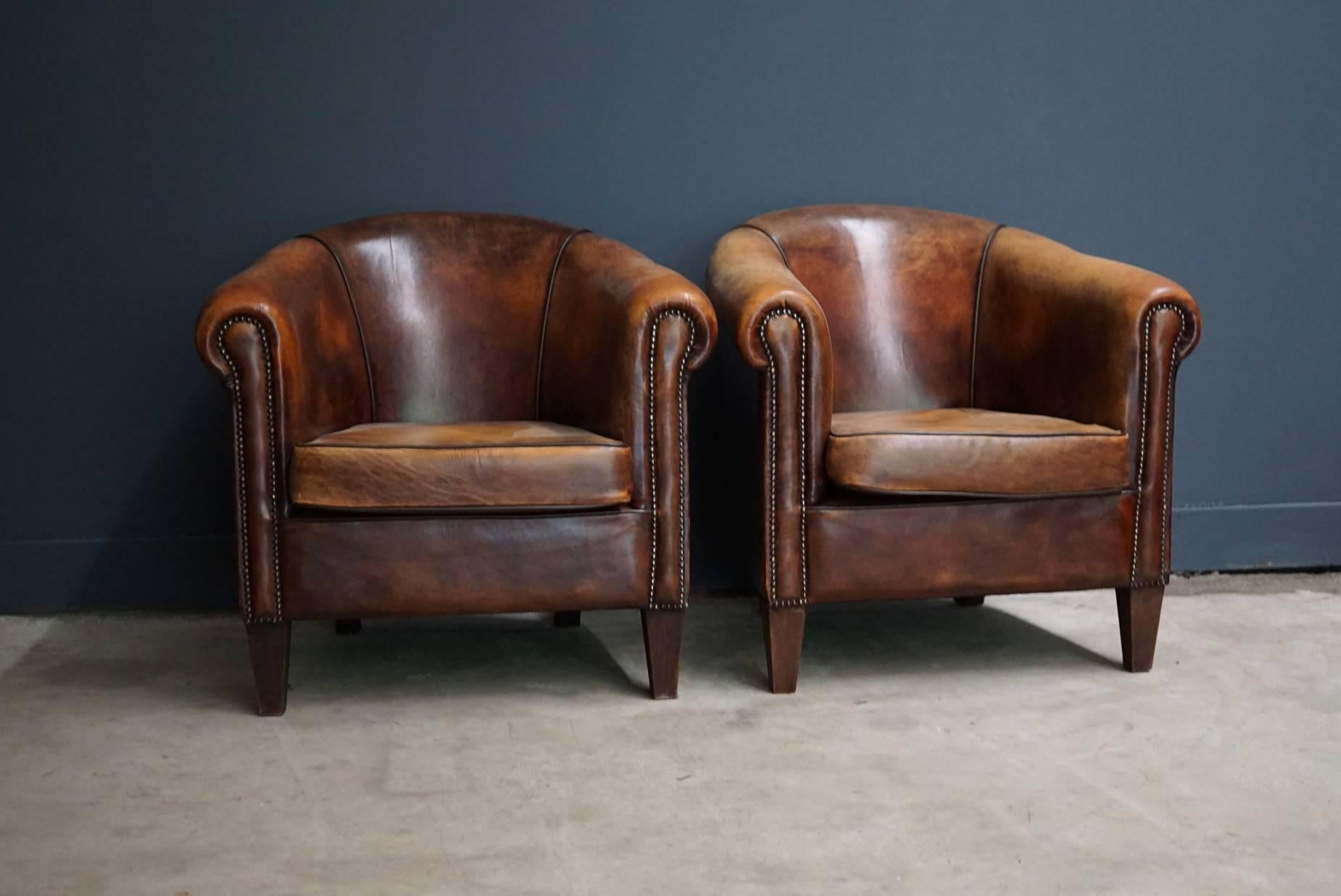 This pair of cognac-colored leather club chairs comes from the Netherlands. They feature rivets and wooden legs.
