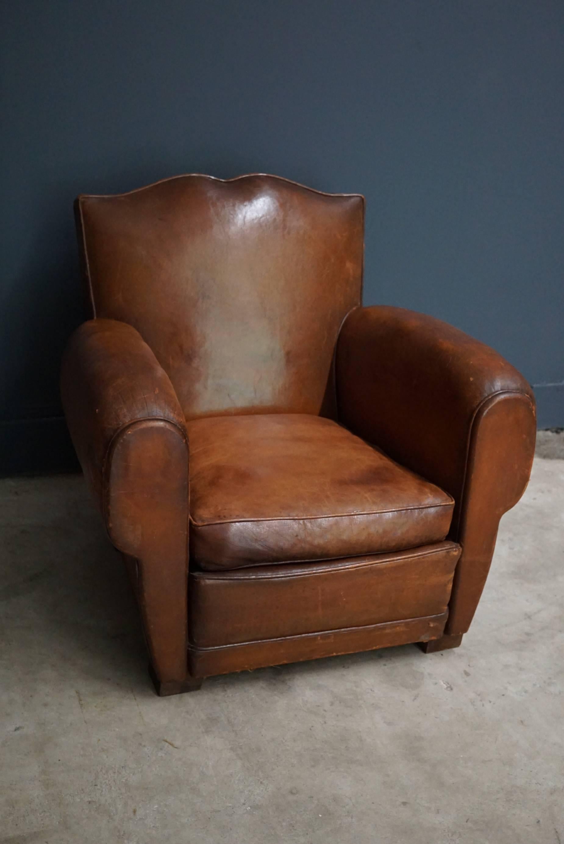 This club chair was designed and produced in France during the 1940s. It is made from cognac leather held together with metal pins and mounted on wooden legs.