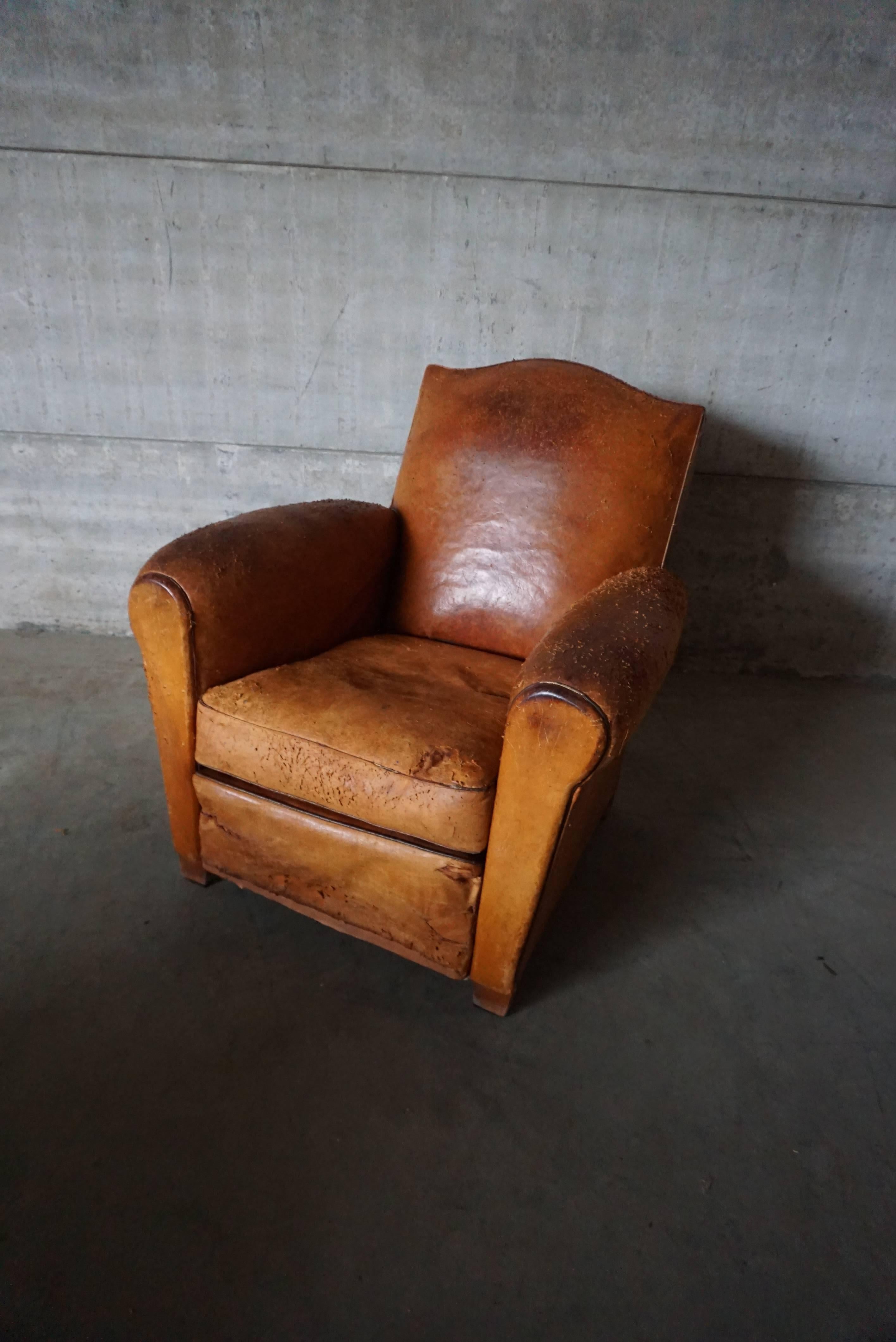 This club chair was designed and produced in France during the 1930s. The chair is made from cognac leather held together with metal pins and mounted on wooden legs. The lounge chair is in fair vintage condition with signs of use and repairs.
