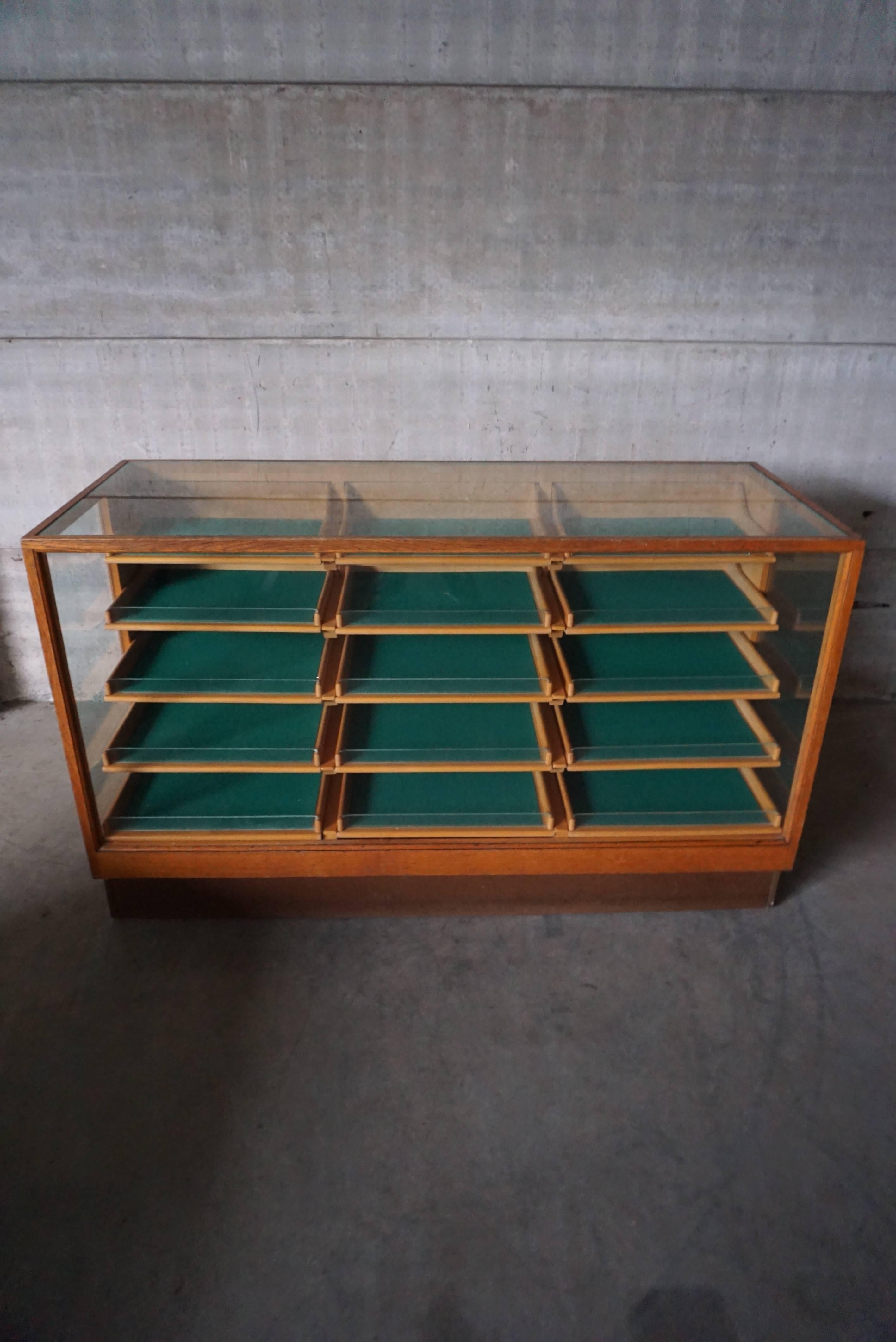 This small shop counter was made and manufactured during the 1950s. It features an Oak frame with pine wood drawers with wooden handles and a glass casing. It remains in a good vintage condition with some marks consistent with age and use.