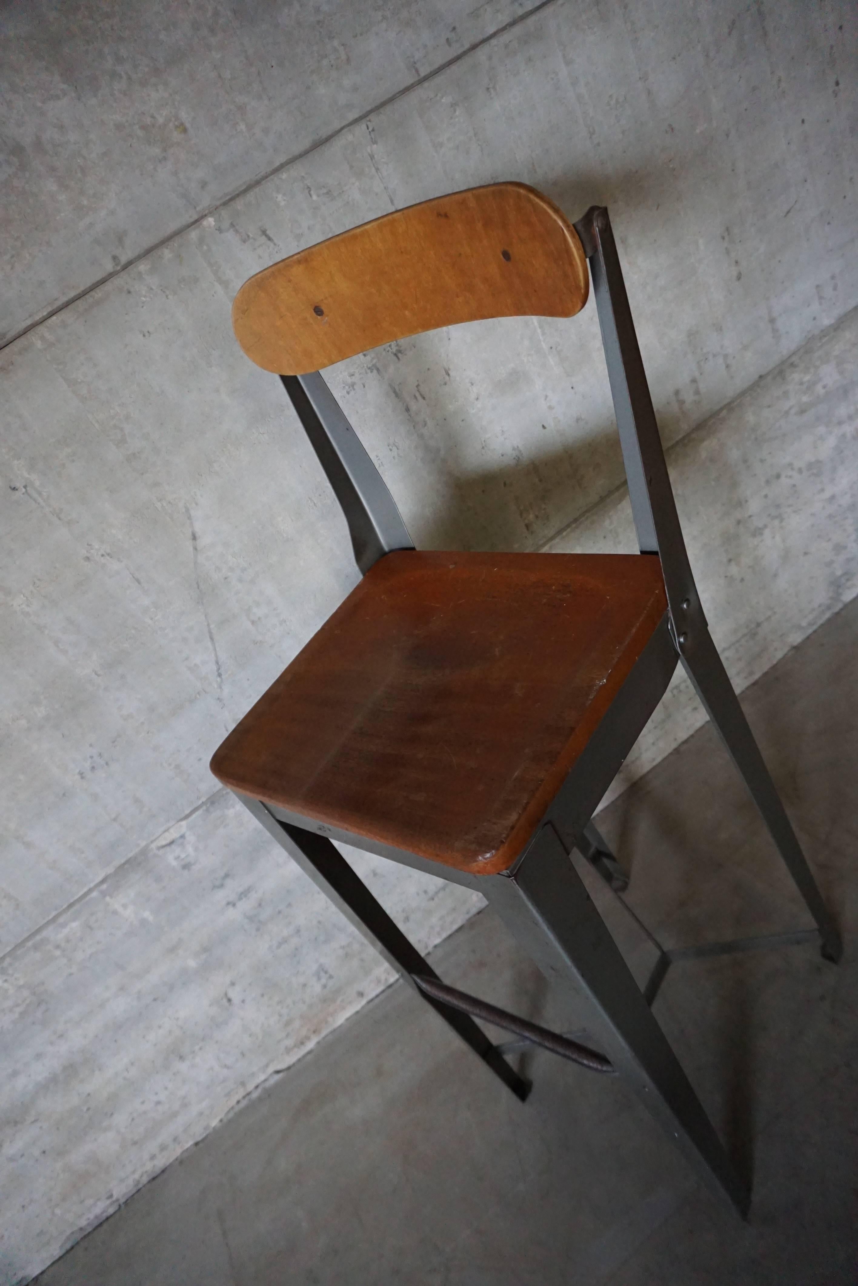 This factory chair was designed and manufactured in England in the 1950s. It features a grey metal frame with wooden seat and backrest. It is in good vintage condition with signs of use. 