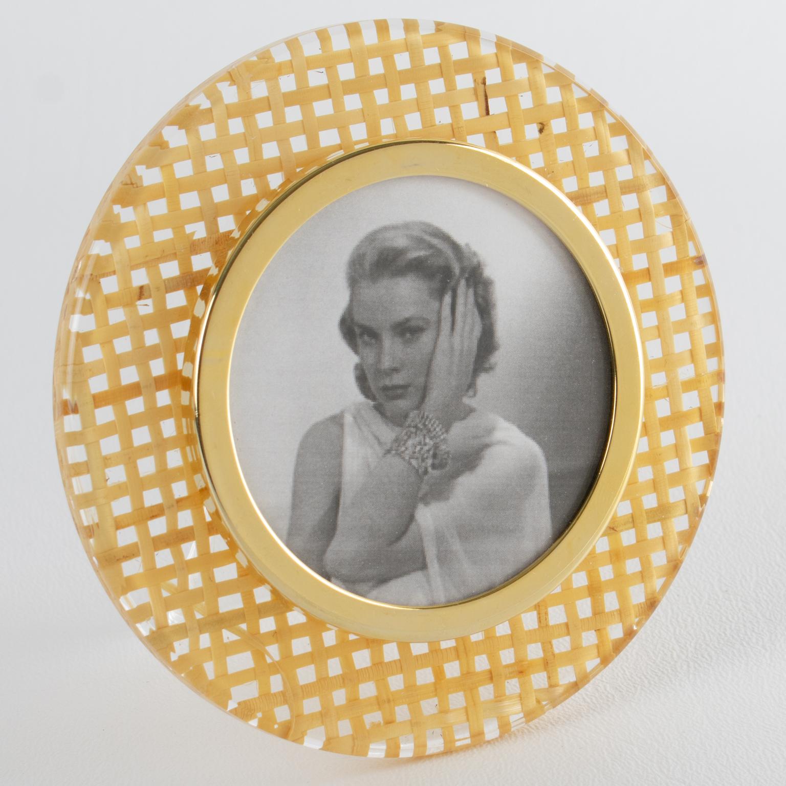 This lovely decorative picture frame is perfect for a living space or vanity. The frame features a rounded shape with clear Lucite and rattan or wicker cane work. The rattan is embedded within the Lucite material. The photo view is surrounded by