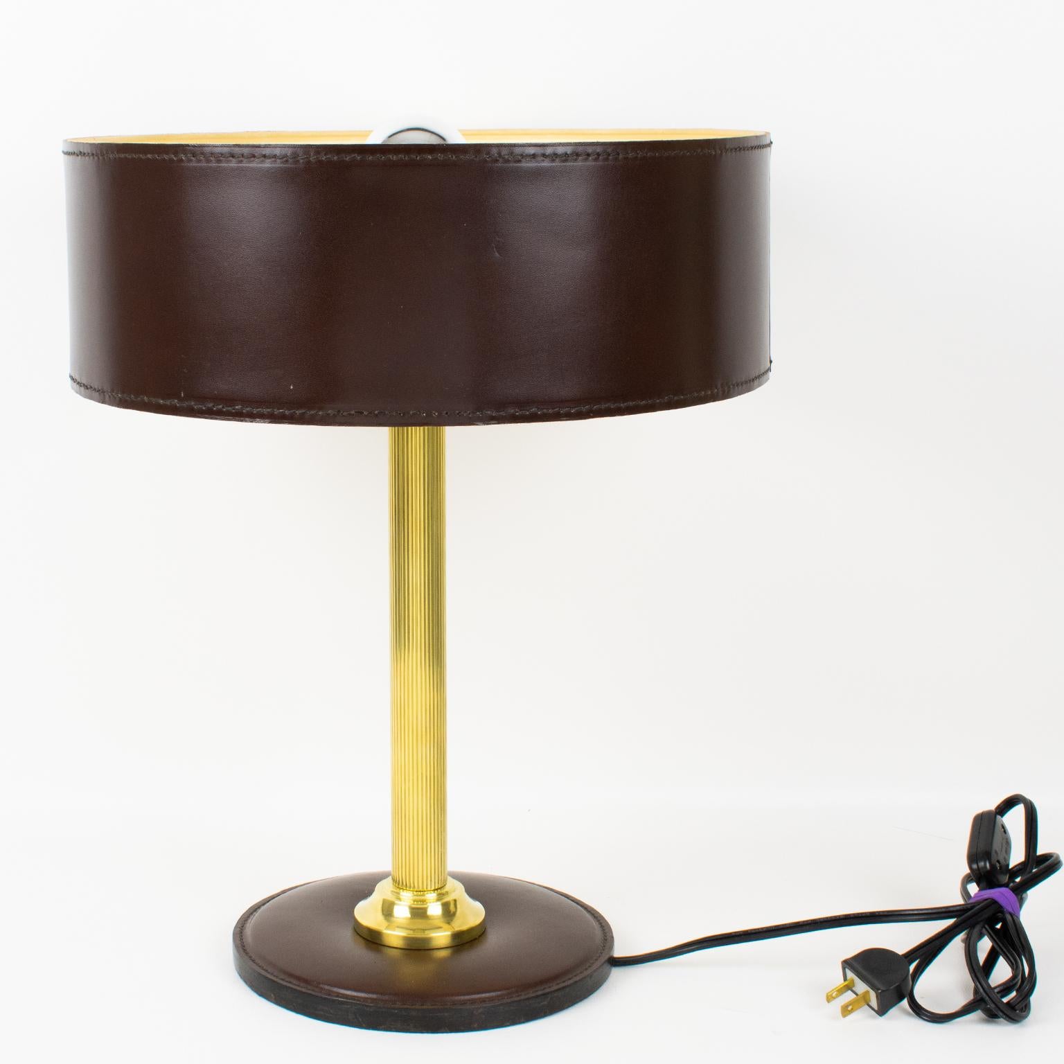 This stunning table lamp was designed by French designer Jacques Adnet (1901-1984). This classical hickory brown color lamp features a hand-stitched shade with ivory paper lining, a polished brass reeded column stem, and a rounded base in the same