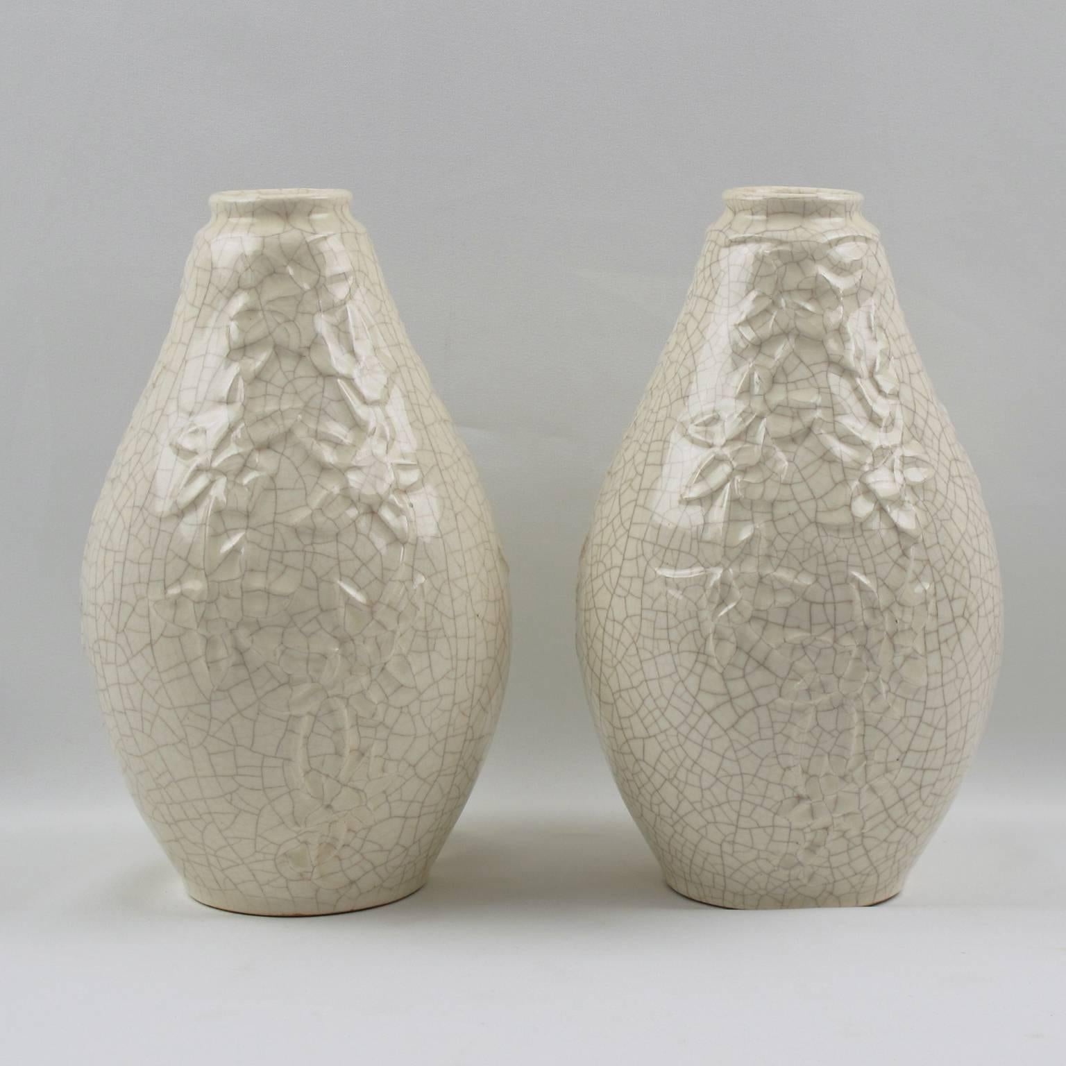 Stunning pair of Art Deco vases by Saint Clement, France. Ceramic vases with white crackle glaze finish. Features an elongated squash shape with narrow opening and garland of flowers design in a stylized pattern (three designs all around). 
The