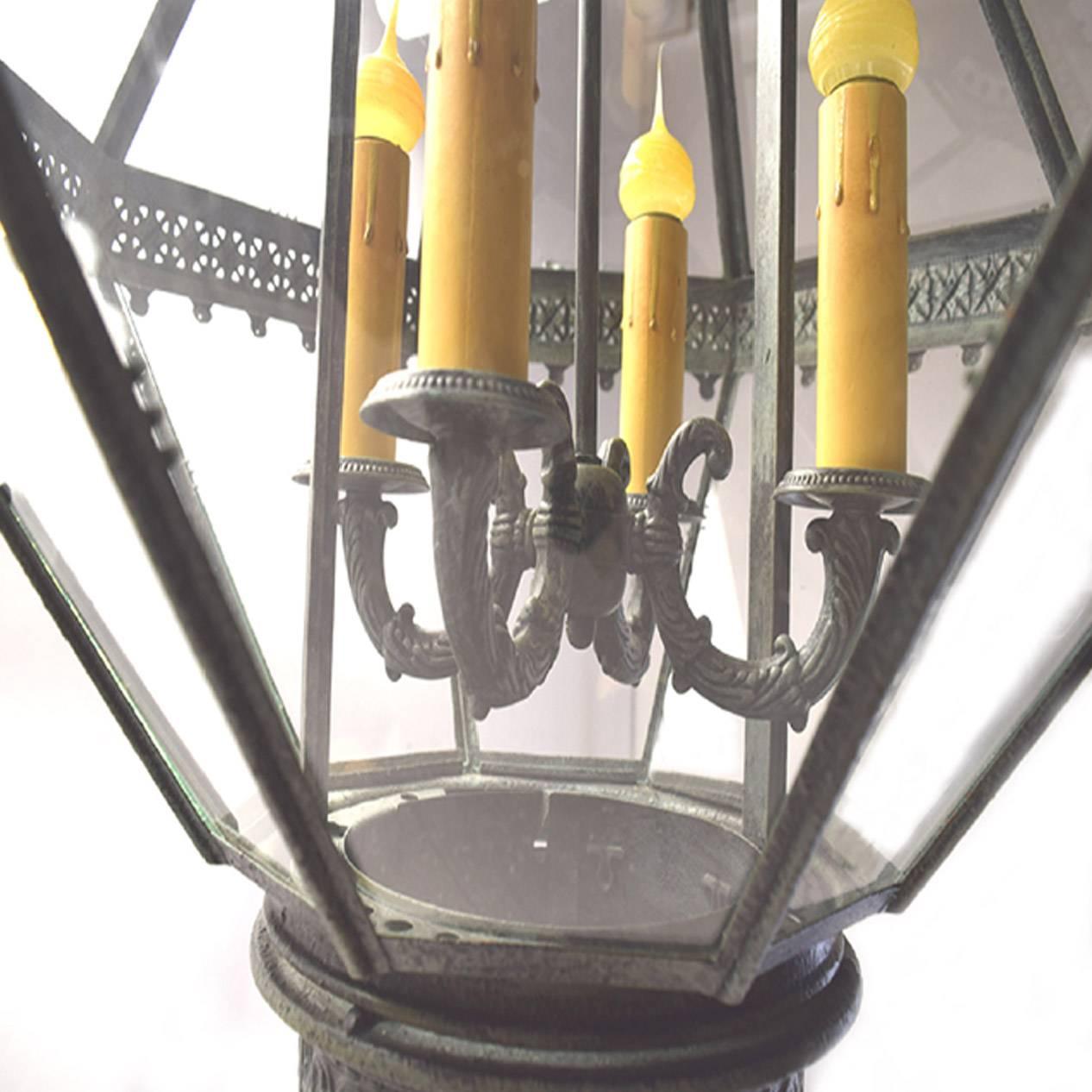 Antique French Napoleon III period cast iron and tole peinte hanging lantern; with a cylindrical paneled corona over an octagonal body of two rows of tapered glass panels with a pierced girdle, congaing four candle arms, over a circular base with