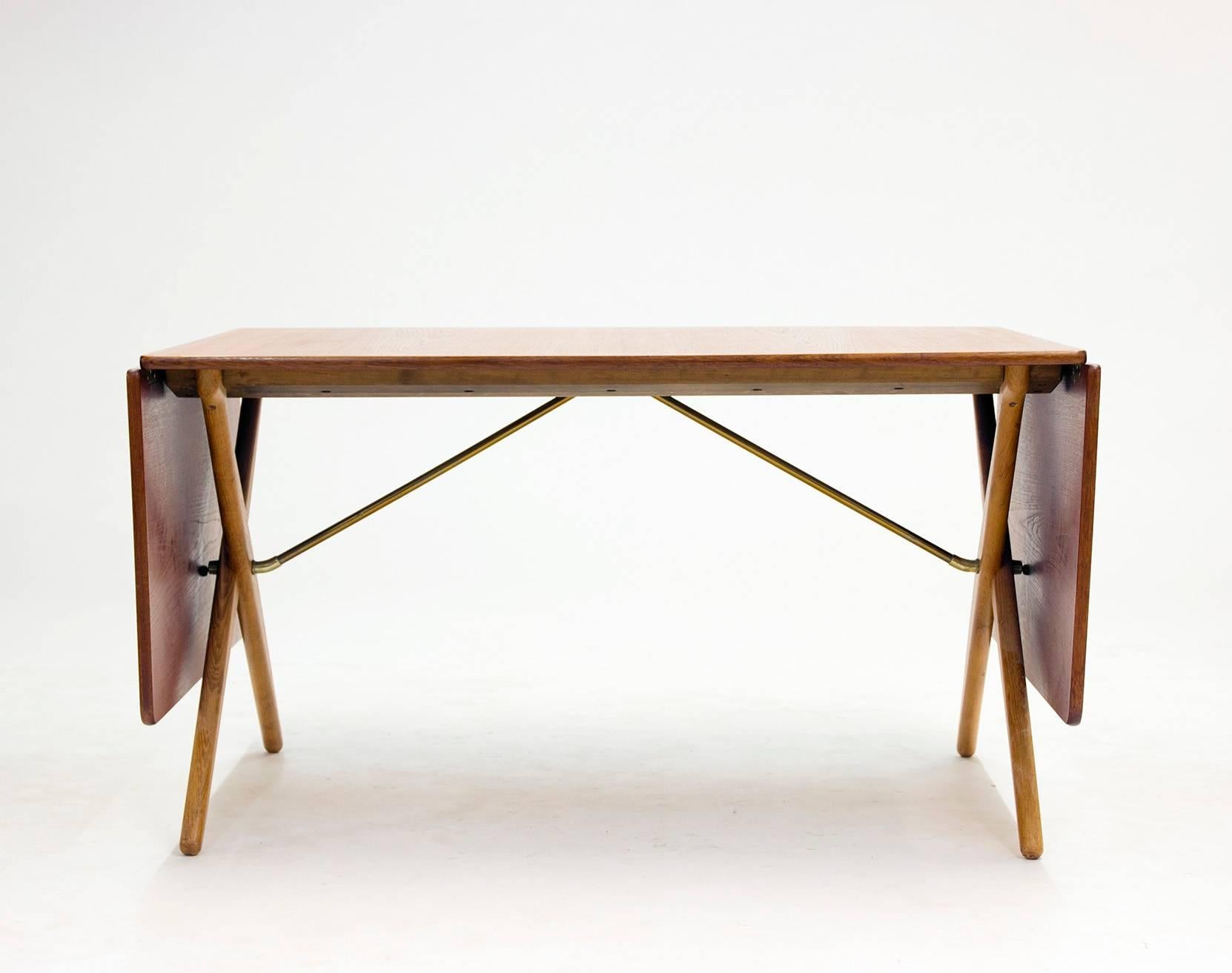 Cool dining table with crossed legs and two flaps that fold out by Hans J. Wegner, model "AT303." Teak table top and oak legs, brass stretchers underneath creating a nice detail.

Drop-leafs are 50 cm each.
