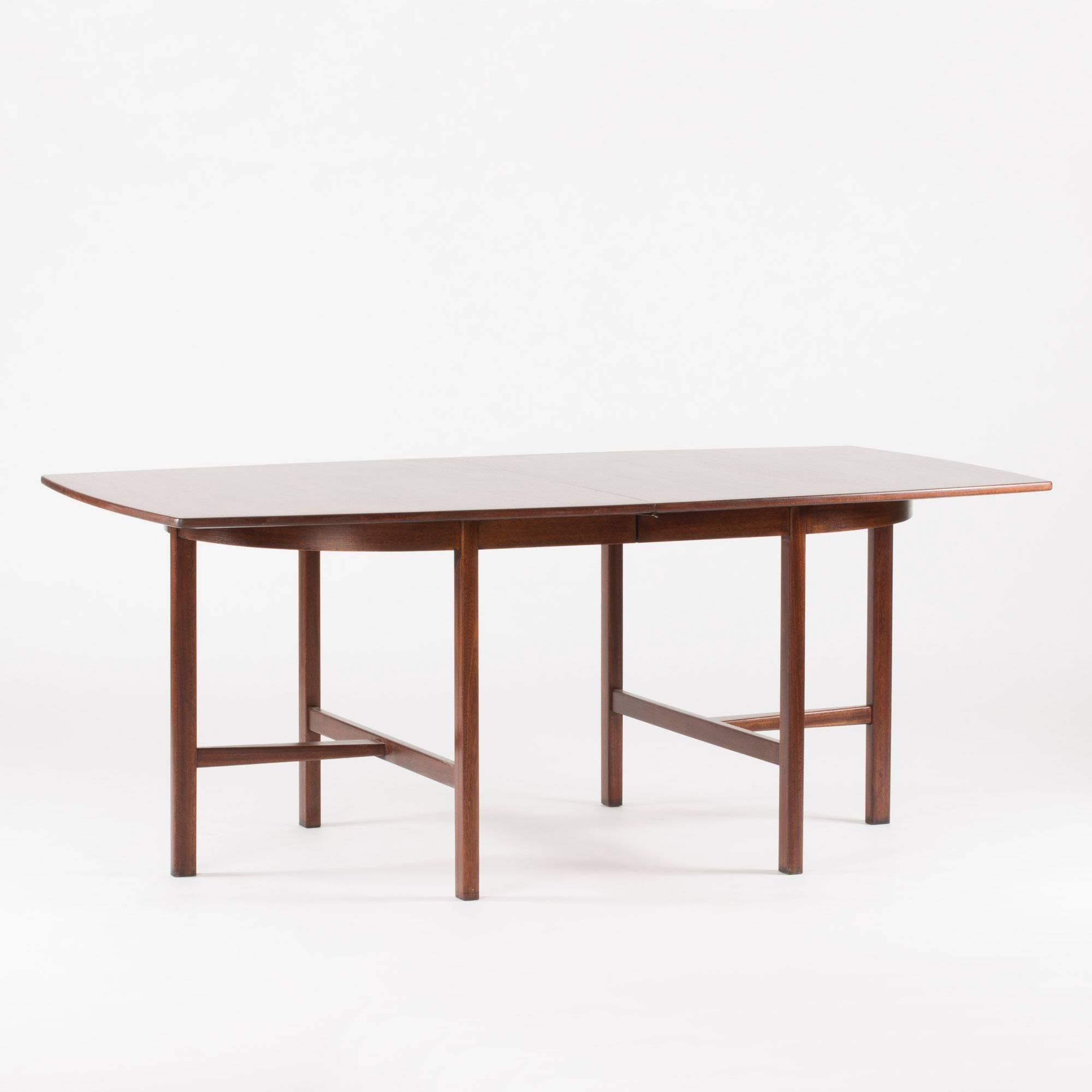 Mahogany dining table by Carl-Axel Acking, with strict, T-shaped legs. The middle bars of the Ts narrow off with subtle elegance where they meet the top bars. The table includes two extra leaves, each 55 cm long, that extends it to a total length of