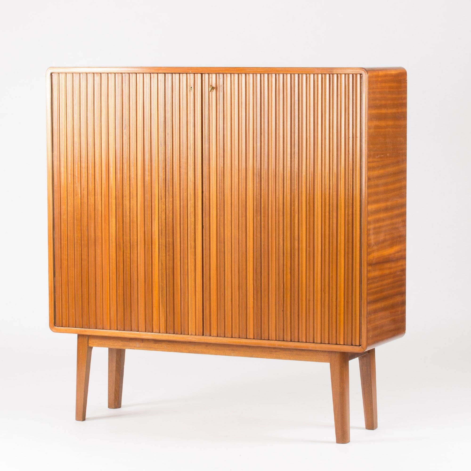 Stunning mahogany cabinet by G.A. Berg, in a square shape with slightly rounded corners. The doors are decorated with a relief of softly curved stripes that contrasts elegantly with the horizontal veneer on the sides. Shelves and drawers inside, one