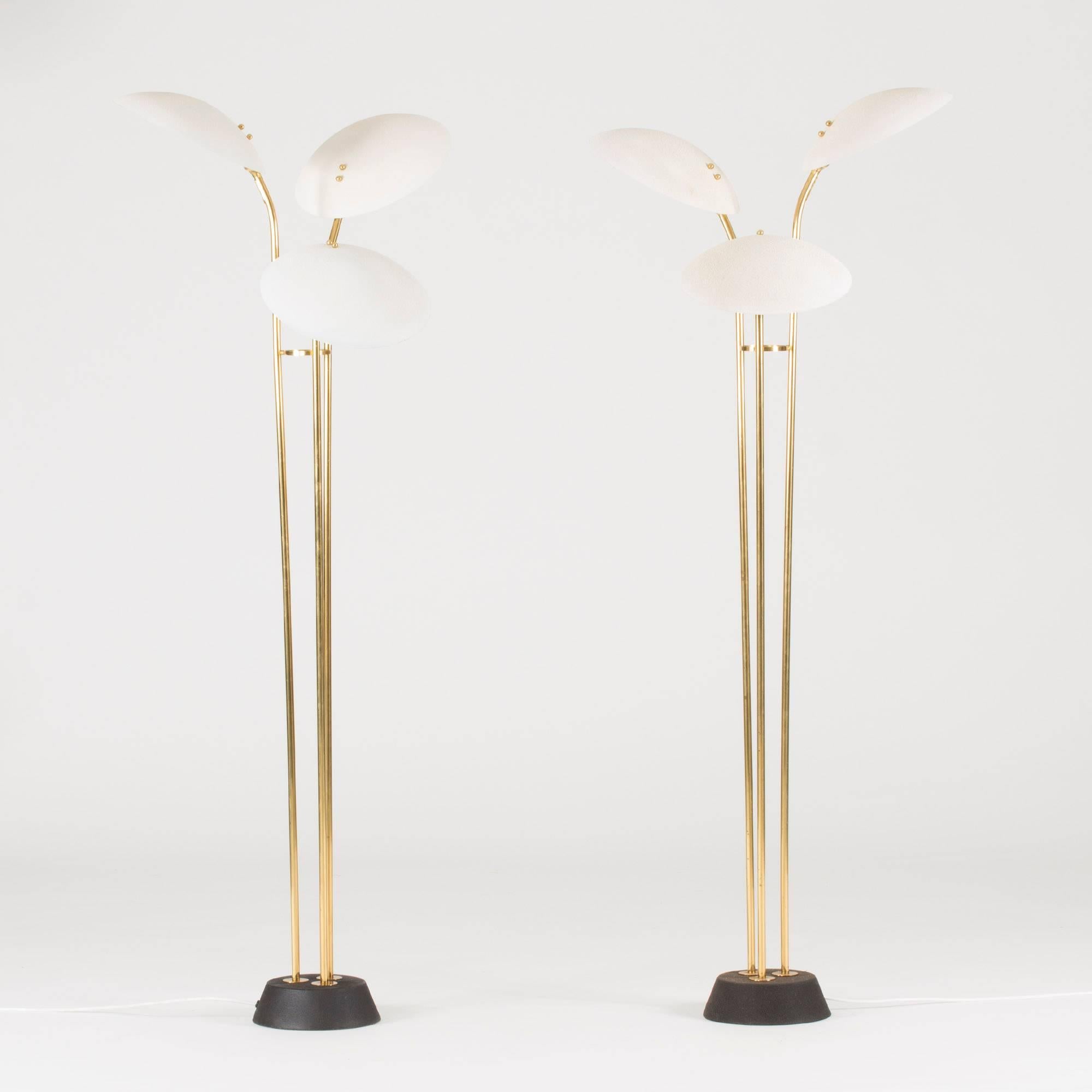 Pair of amazing brass floor lamps from Malmö Metallvarufabrik. Each lamp has three white lacquered circular shades decorated with little brass balls that hide the screws. Black lacquer on the bases.