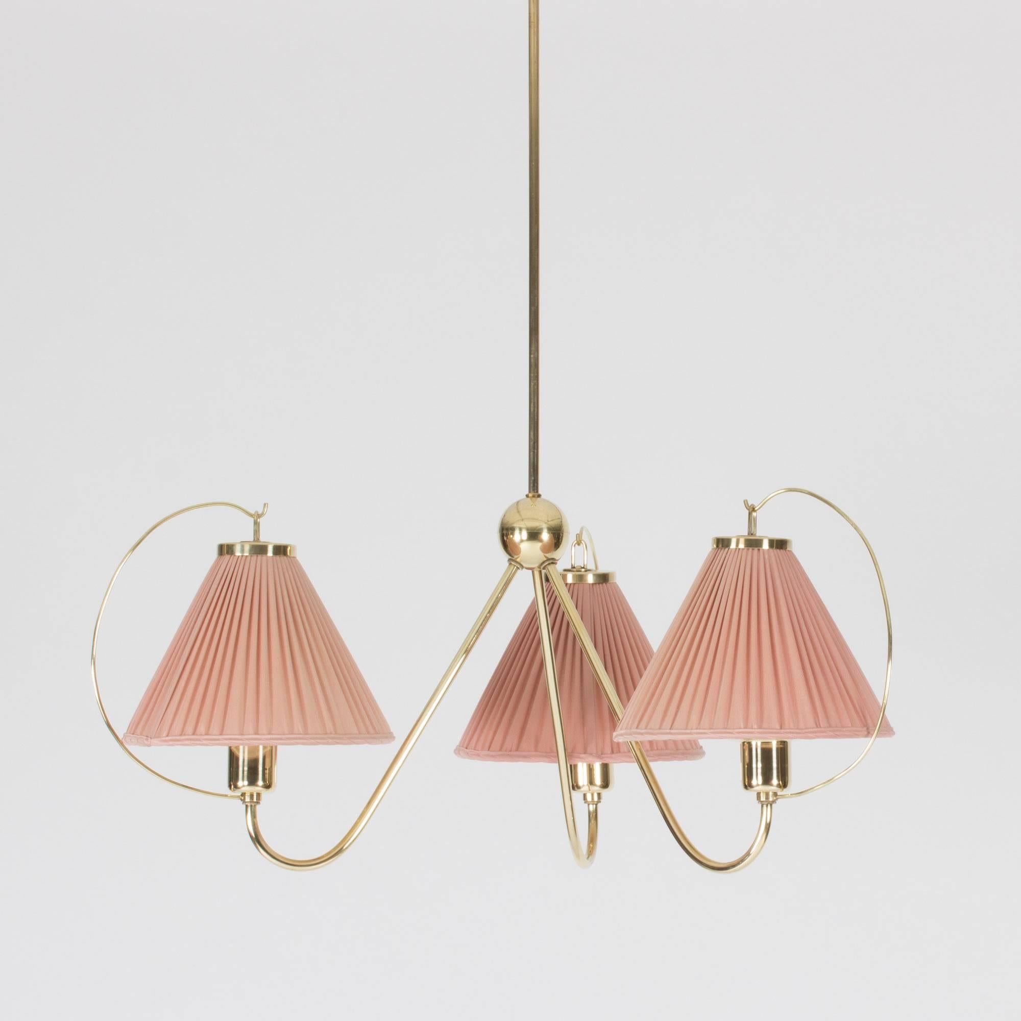 Amazing ceiling lamp by Josef Frank, made from brass with three shades in original dusty pink fabric. Beautiful, slender design where the three arms plunge from a brass globe in the centre. Arched brass strands extend from the sockets and suspend