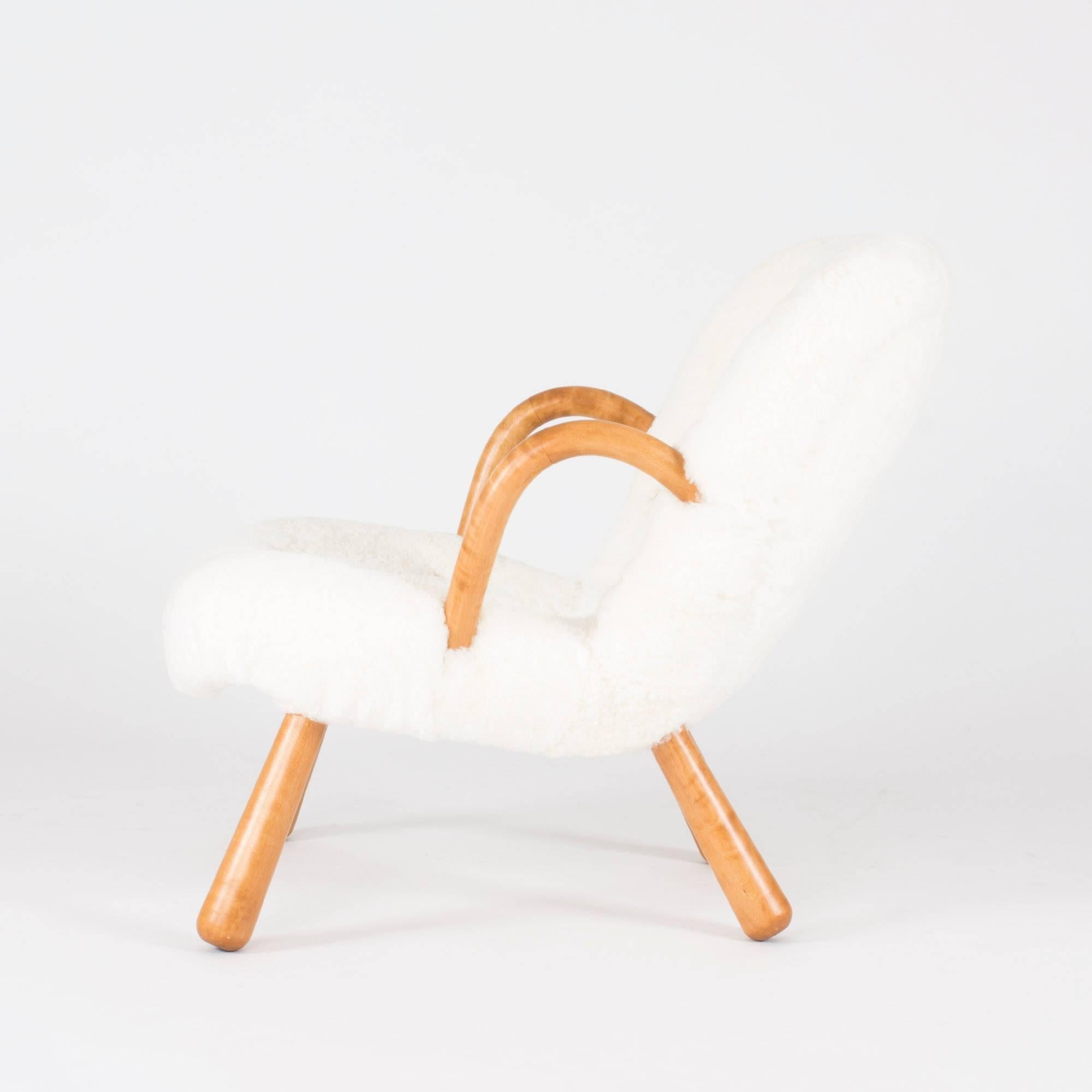 Incomparably inviting “Clam Chair” lounge chair by Philip Arctander. Curved wooden armrests and club like legs. Upholstered with fuzzy white sheepskin. The buttons on the backrest are dressed with light brown leather that matches the color of the
