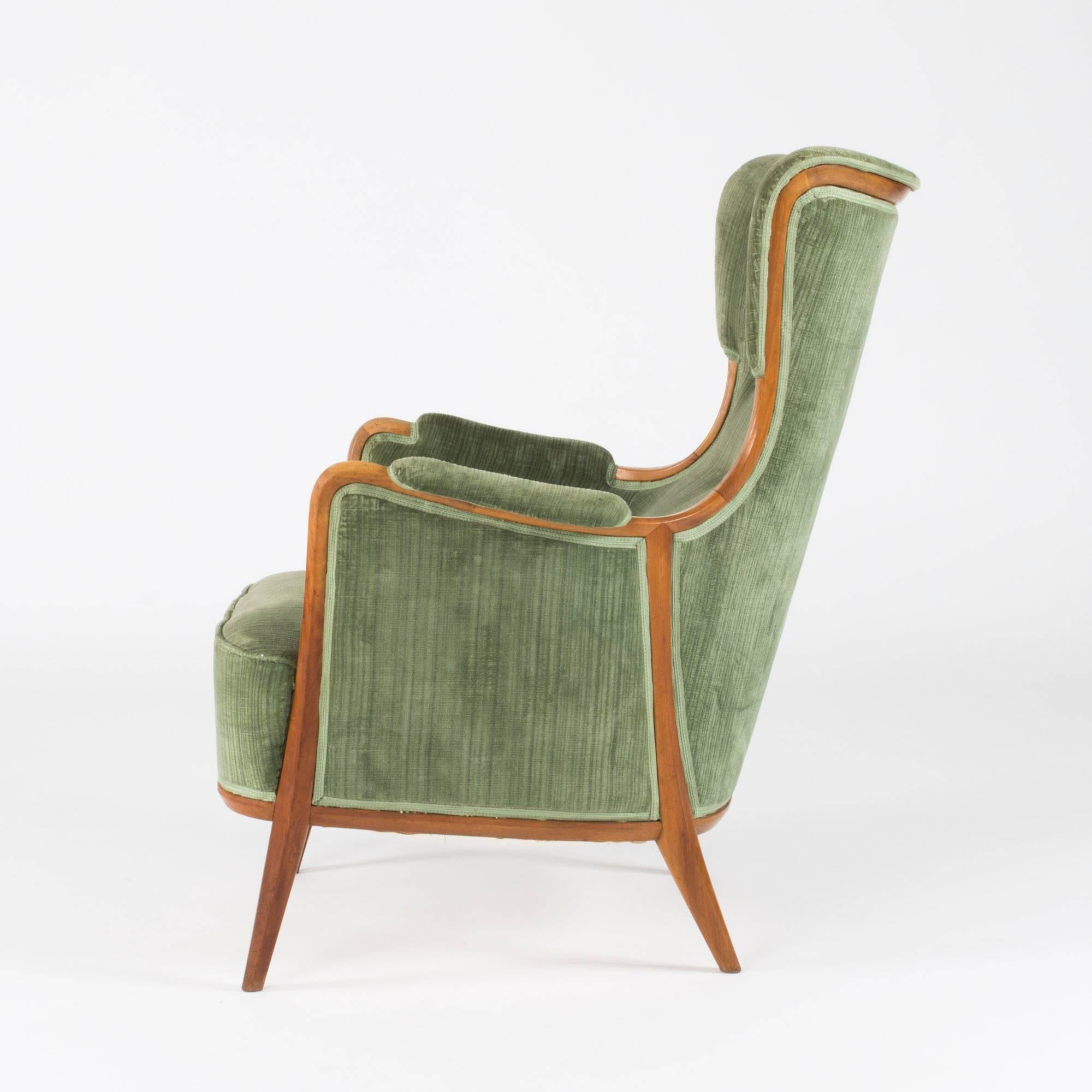 Elegant lounge chair designed by Axel Larsson, executed by master carpenter Hjalmar Jacksson at Stockholms Hantverksförening. Frame made from walnut with a decor of walnut along the edges and forming a pattern on the sides. Original, green velvet