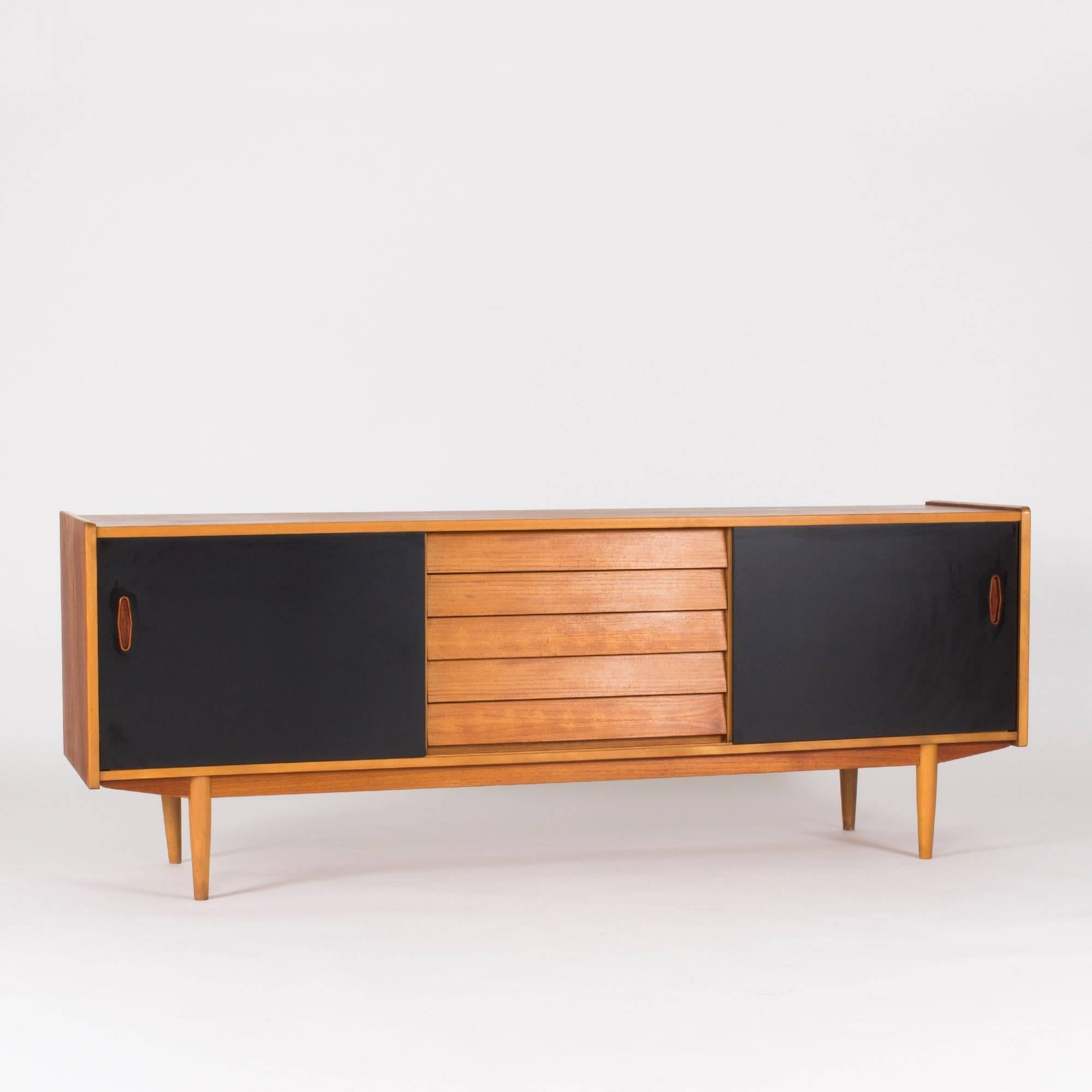 Cool teak sideboard from Hugo Troeds with awesome details. Sliding doors in black with inset teak handles. Drawers in the centre with a graphic relief design. Beautiful condition.