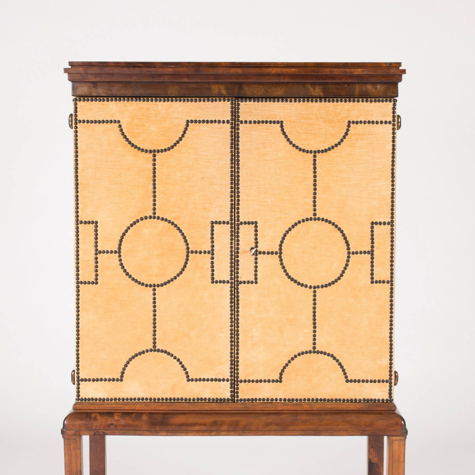 Spectacular cabinet by Otto Schulz, made from stained birch and dressed in a caramel nuance of velvet. Decorated with black metal nails in a geometric pattern. Lion's paw feet.

Otto Schulz was a furniture designer, interior designer, editor and