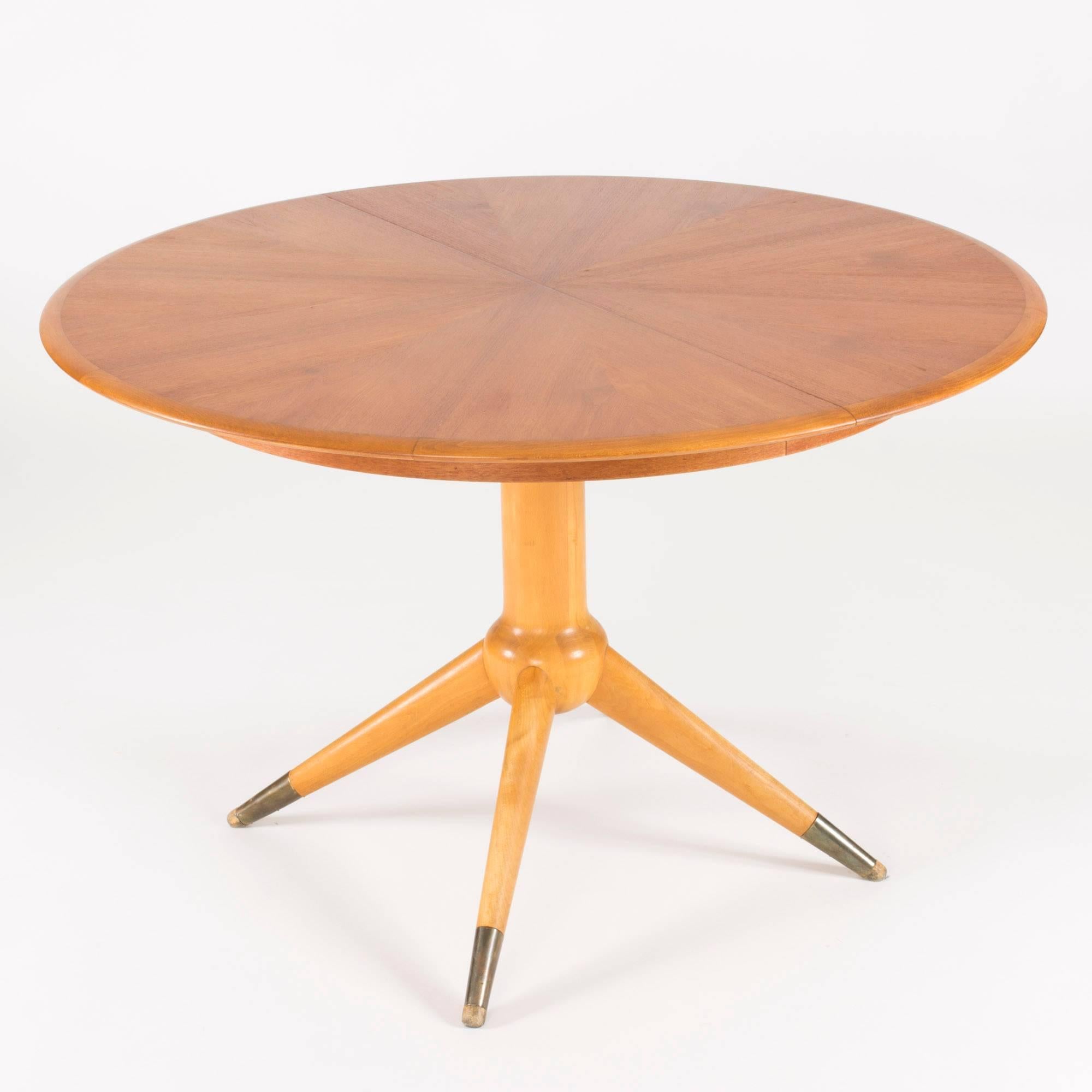 Round teak dining table by David Rosén with a beautiful tabletop where the veneer is laid in a beam pattern from the centre. Piedestal base in beech with feet clad with brass. The table has three extension leaves measuring 45 cm each. When the third