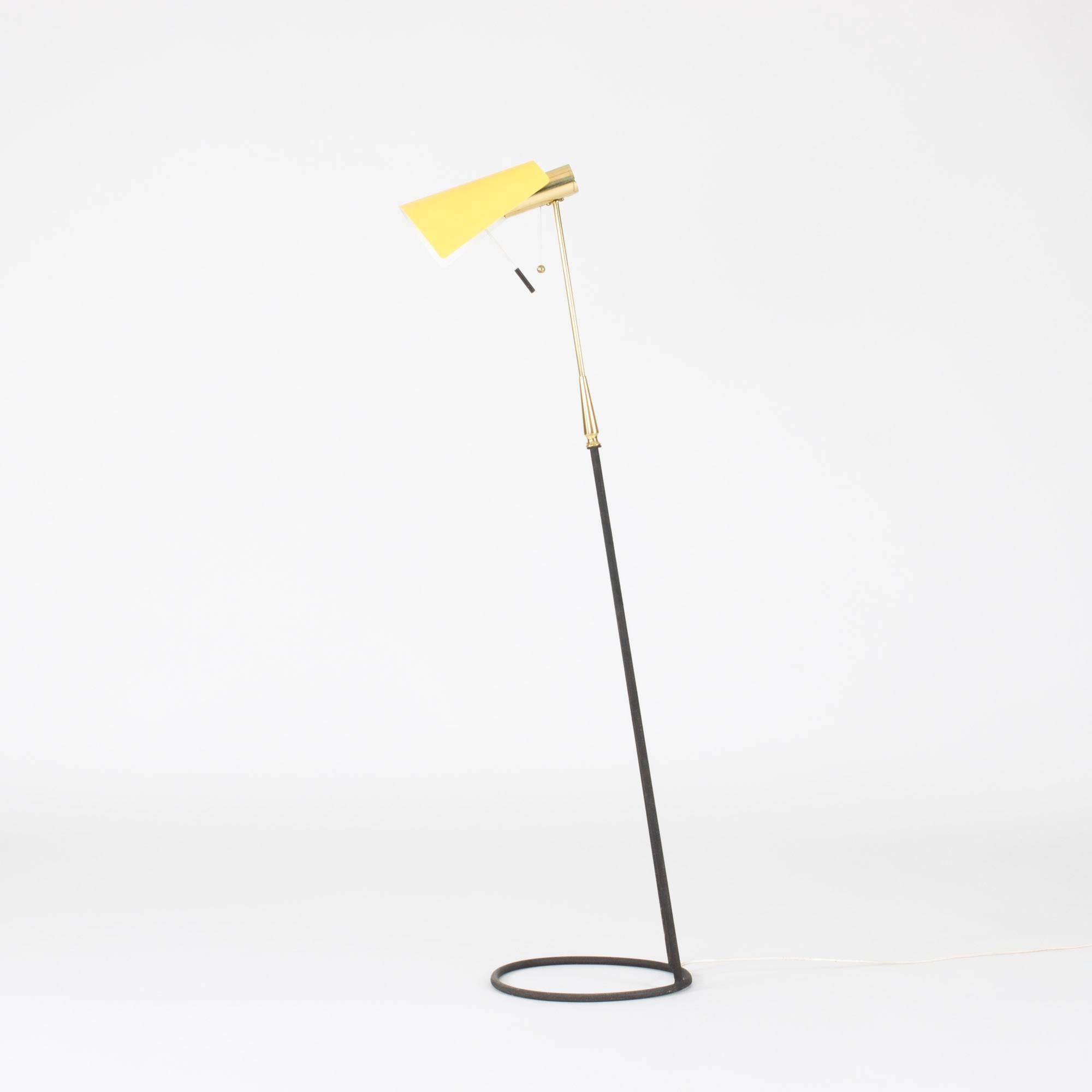 Amazing floor lamp from Falkenbergs Belysning with a brass handle and black metal base with a structured surface. Base shaped like a hoop, somewhat like a musical note, against the floor. Bright yellow metal shade with white inside, adjustable up