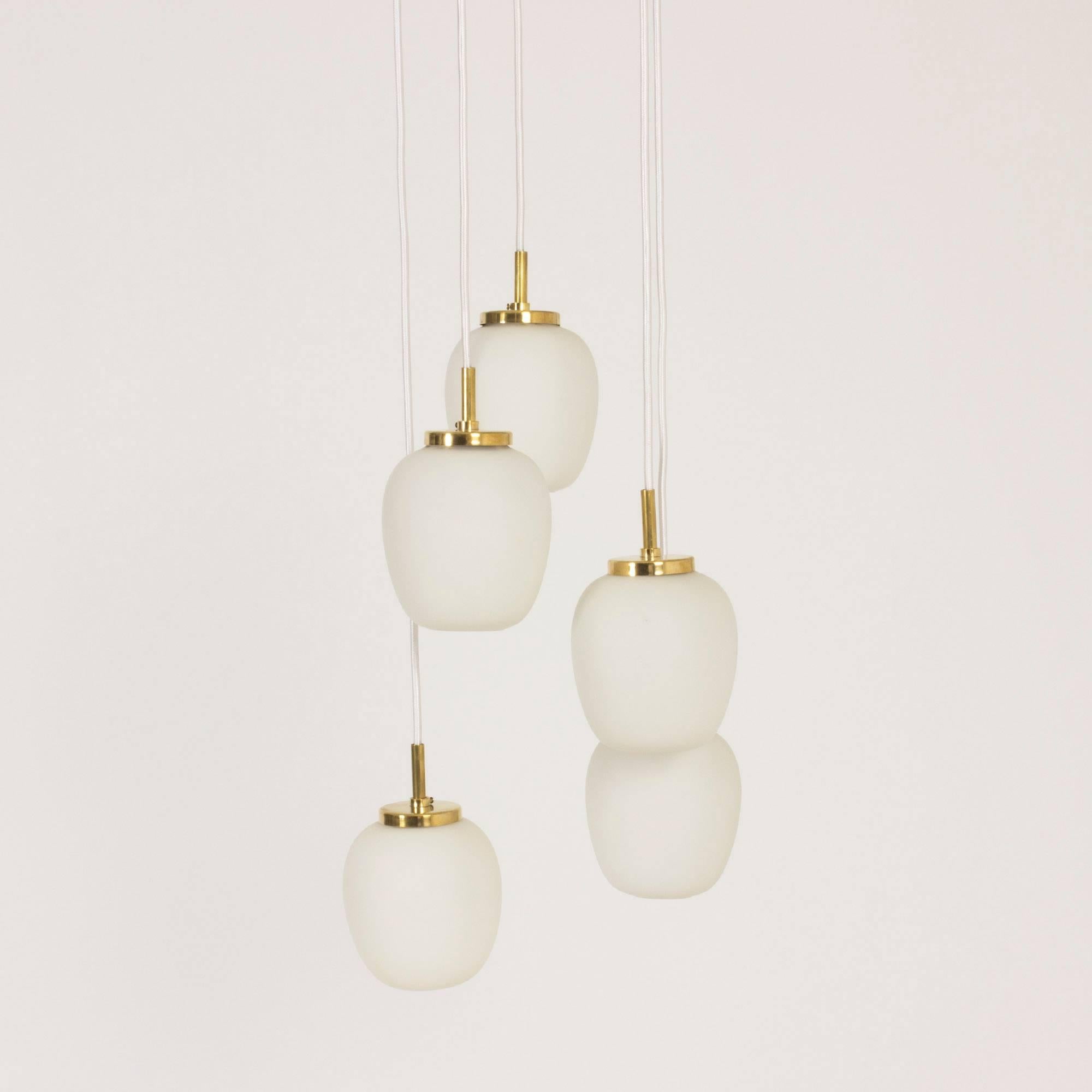 Lovely pendant lamp with five opaline glass shades suspended from a brass ceiling canopy with arms for the five cords. White textile cords.